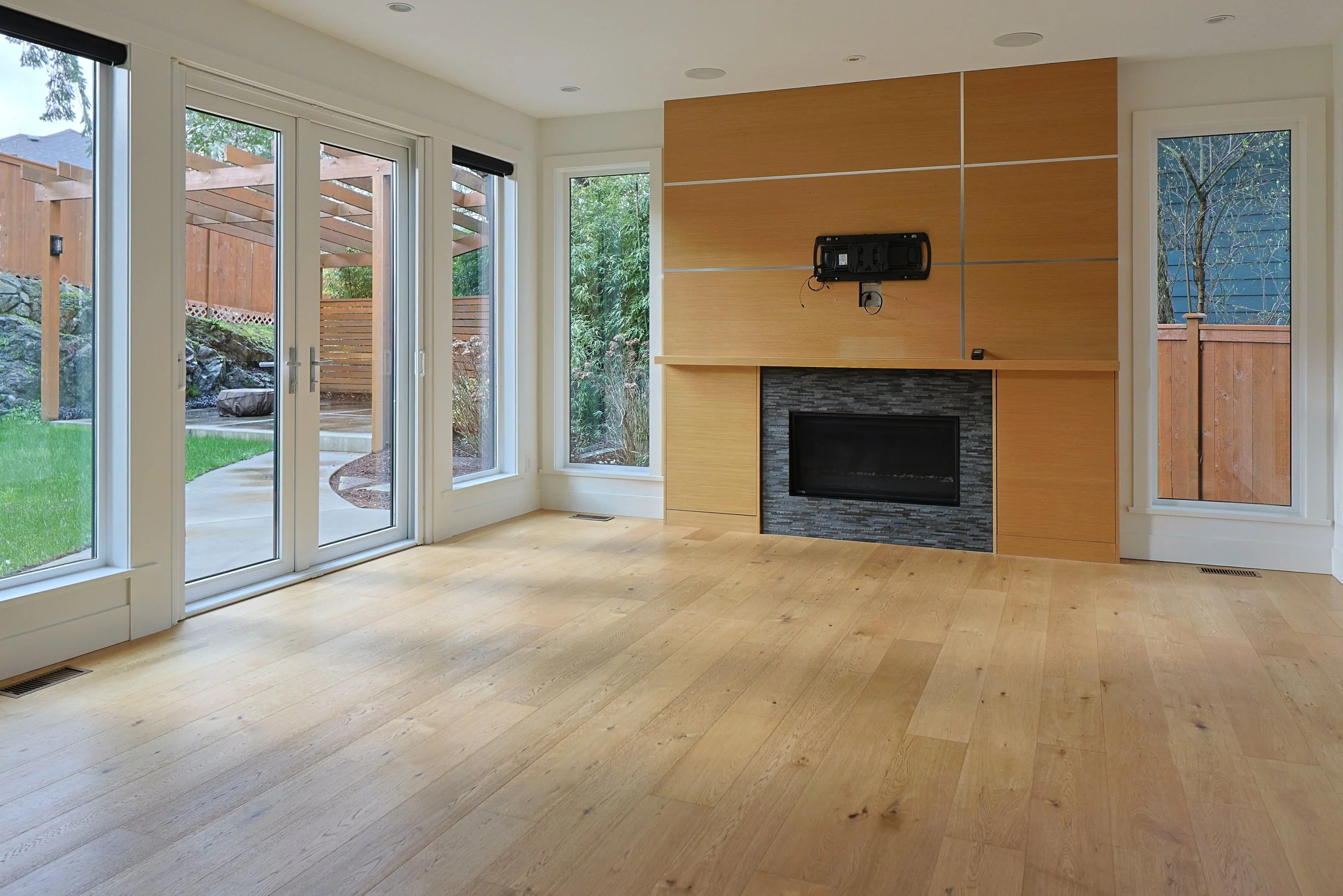 Living room with large glass doors leading outside, wooden floors, modern fireplace with a black stone surround, and a wood-paneled wall.