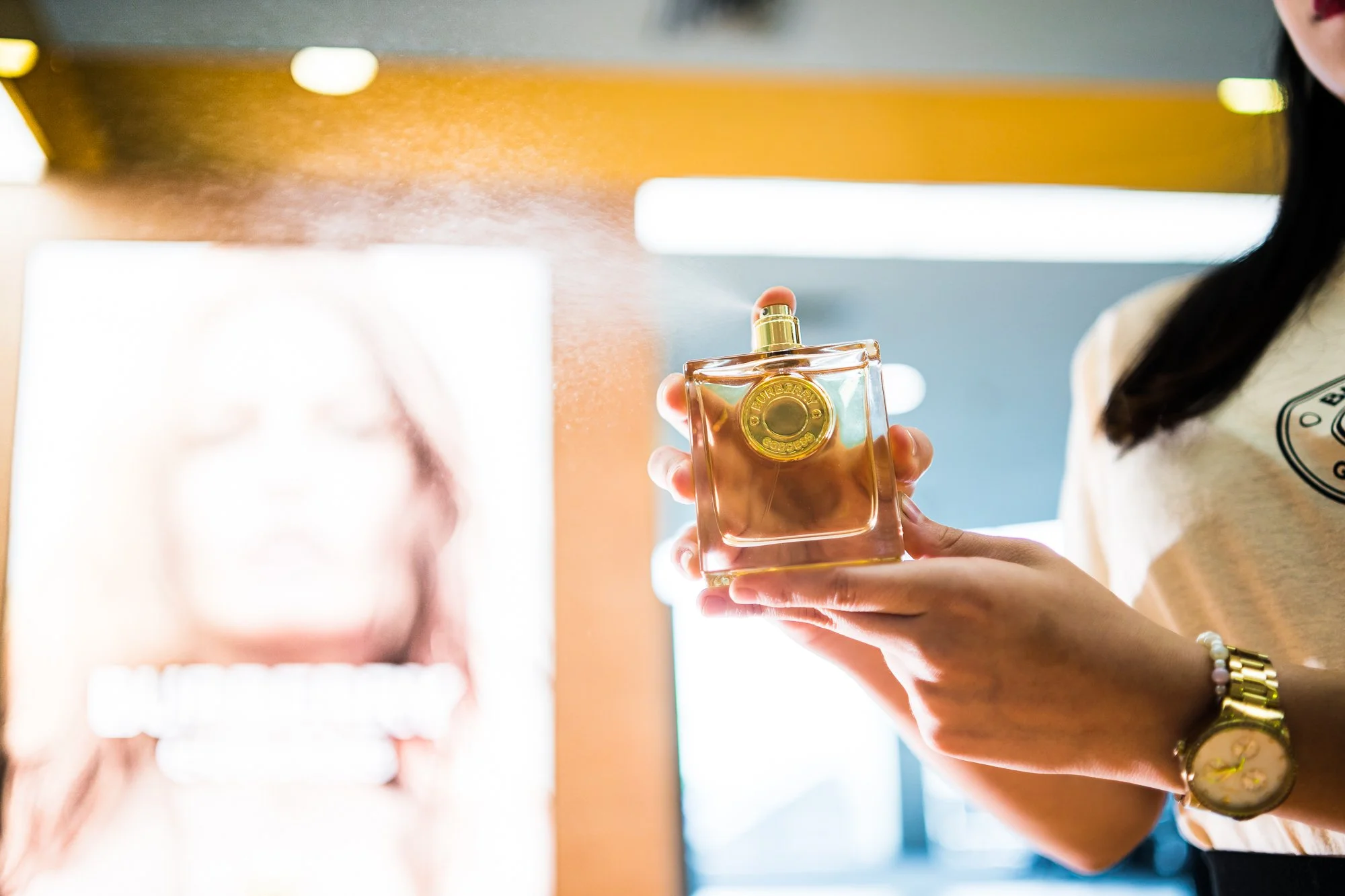Una persona sostiene un frasco de perfume dorado en un entorno con iluminación brillante.