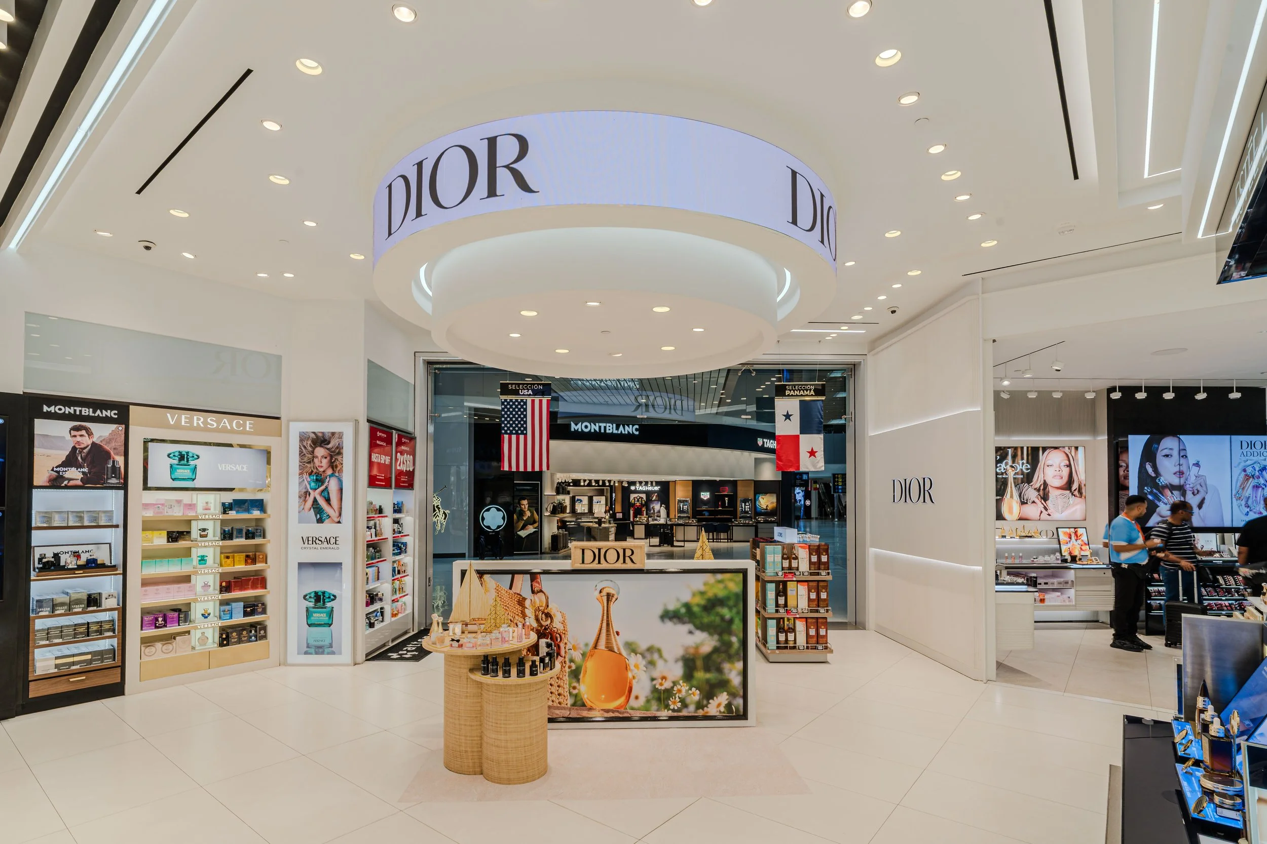 Entrada a una tienda Dior en un centro comercial, con exhibiciones de perfumes y productos de lujo, y varias pantallas digitales.