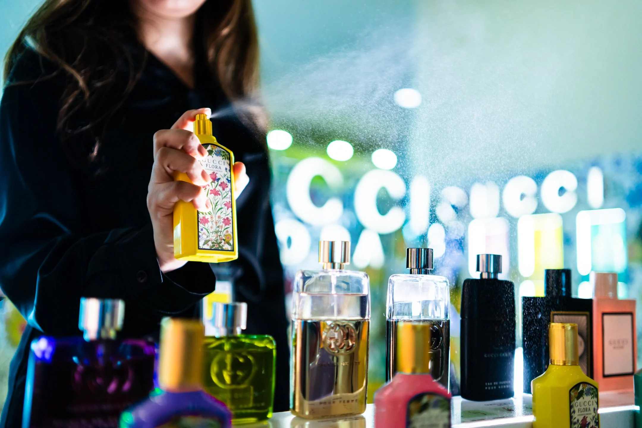 Persona rociando perfume en la tienda, con varias botellas de fragancias en exhibición.