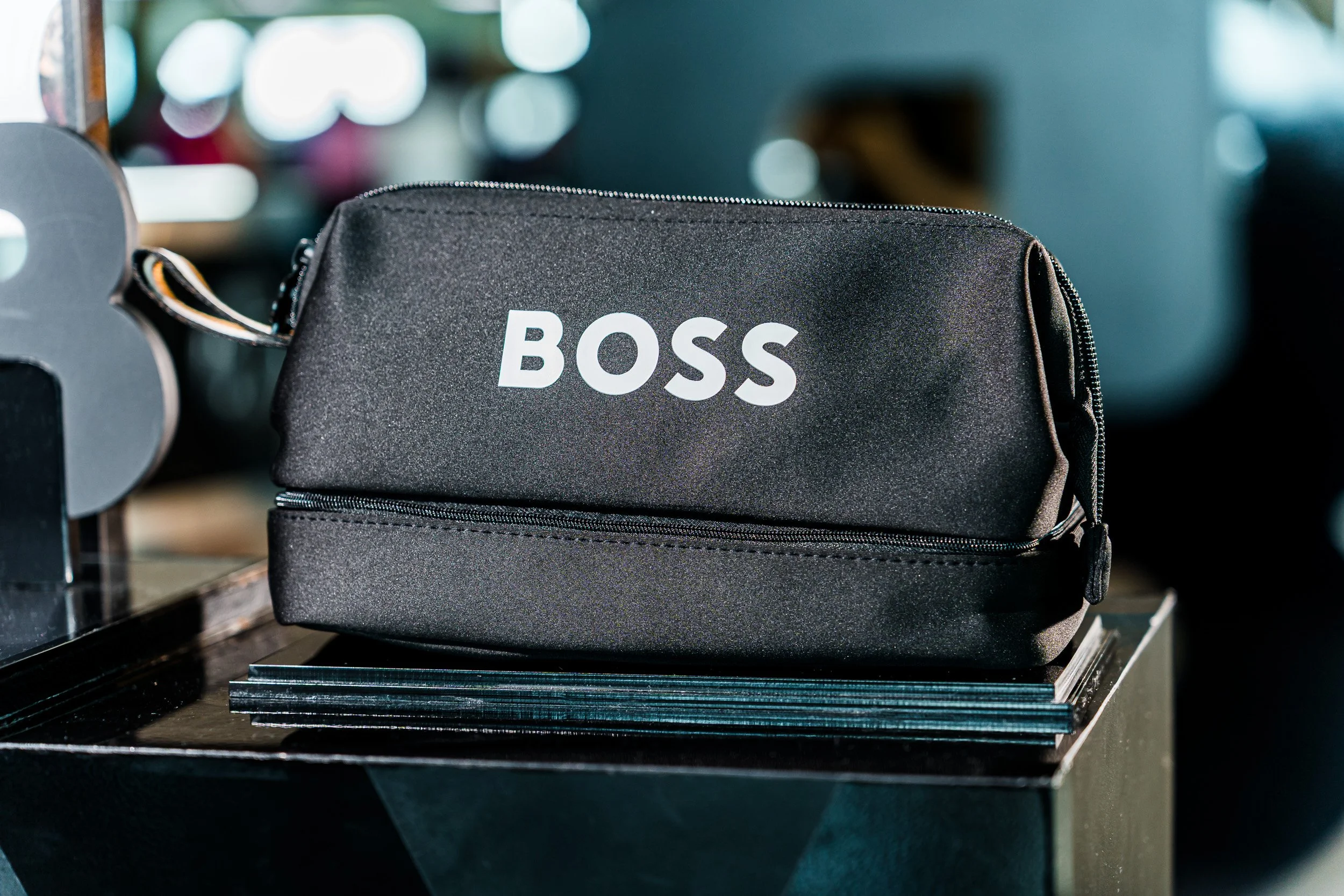 Bolsa negra con la palabra BOSS en letras blancas, colocada sobre una mesa con libros apilados.