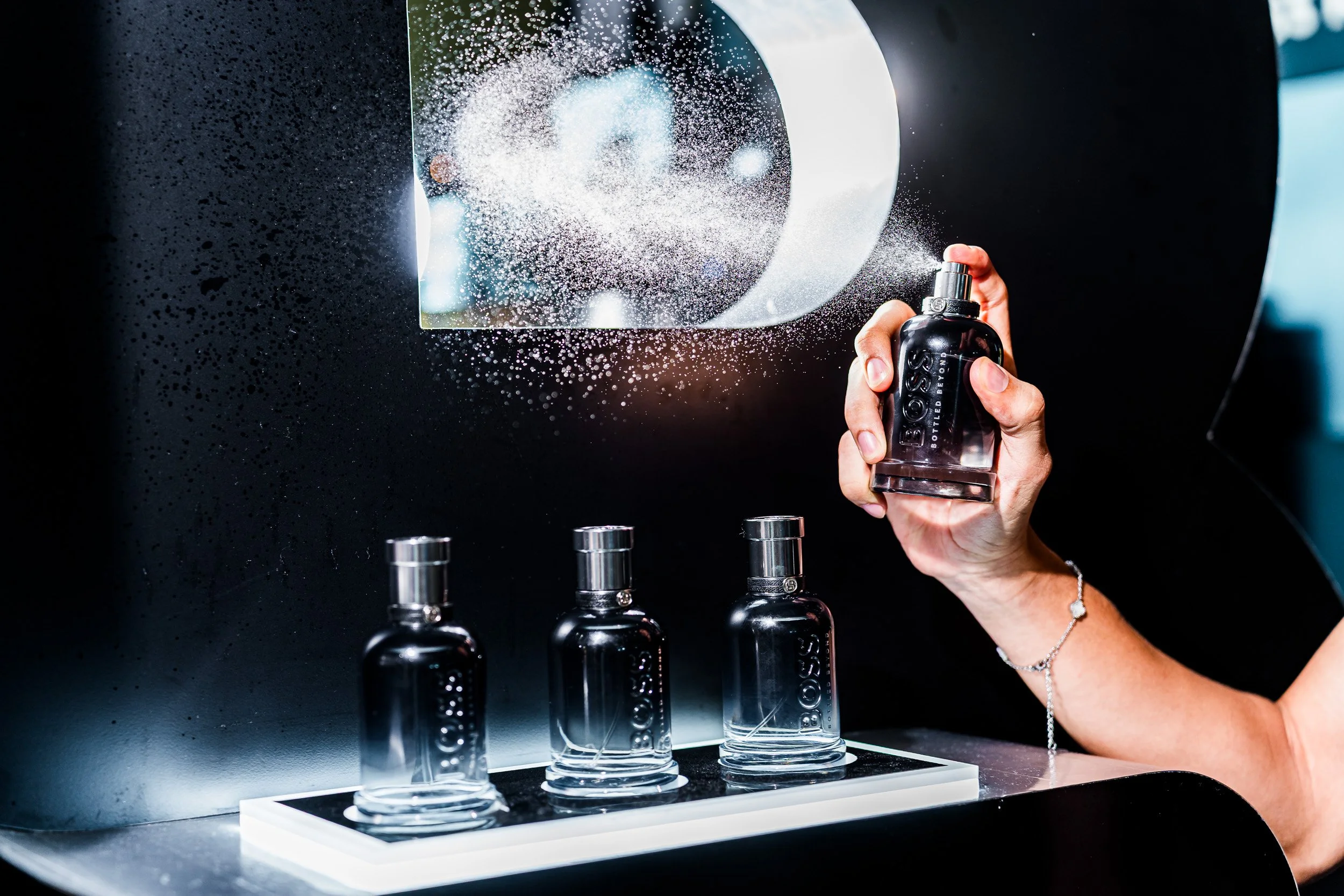 Persona rociando perfume en una muestra de fragancias en un banco con varias botellas de perfume.