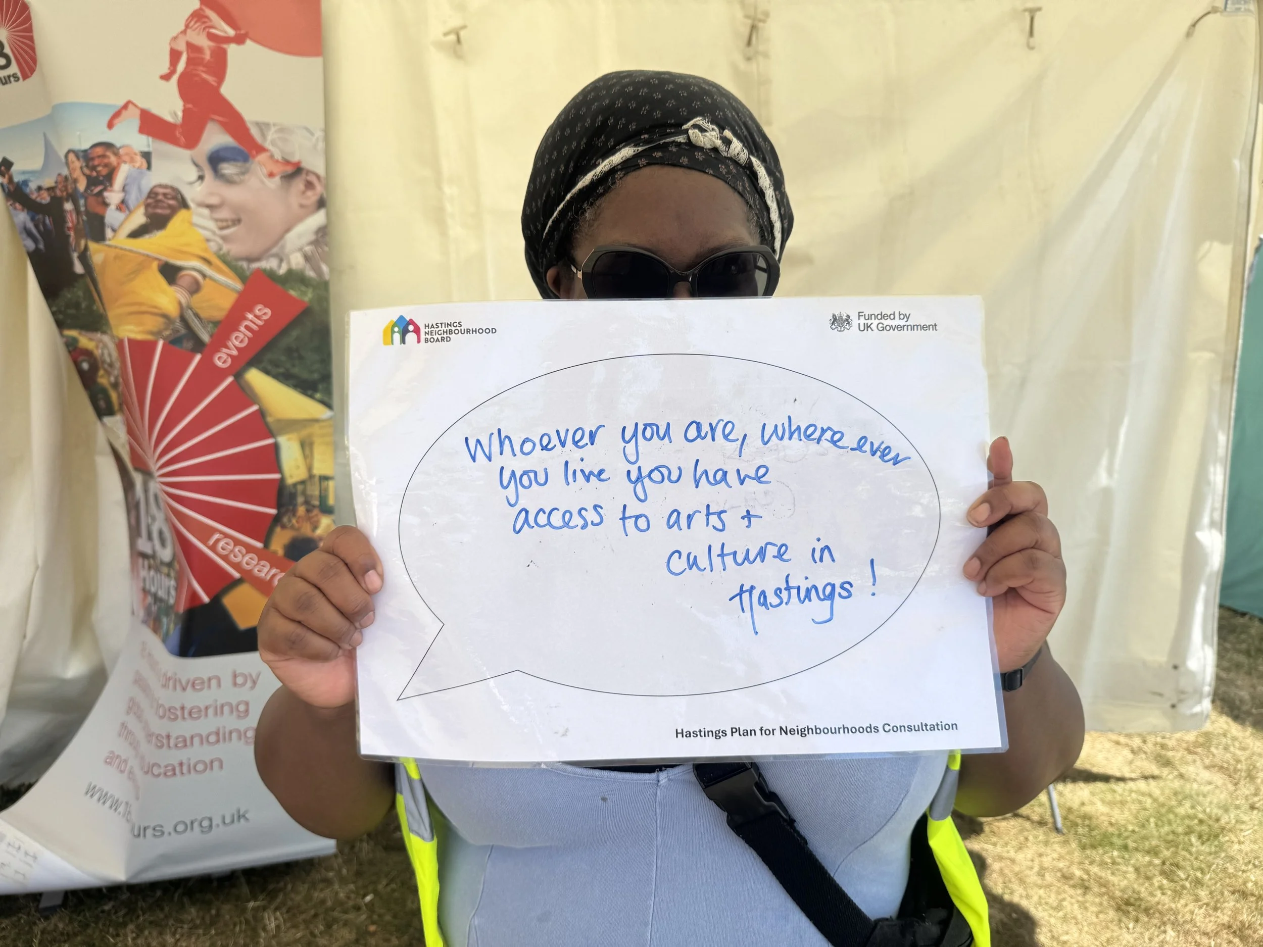 Woman holding a sign which reads 'Whoever you are, wherever you live you have access to arts and culture in Hastings!'.