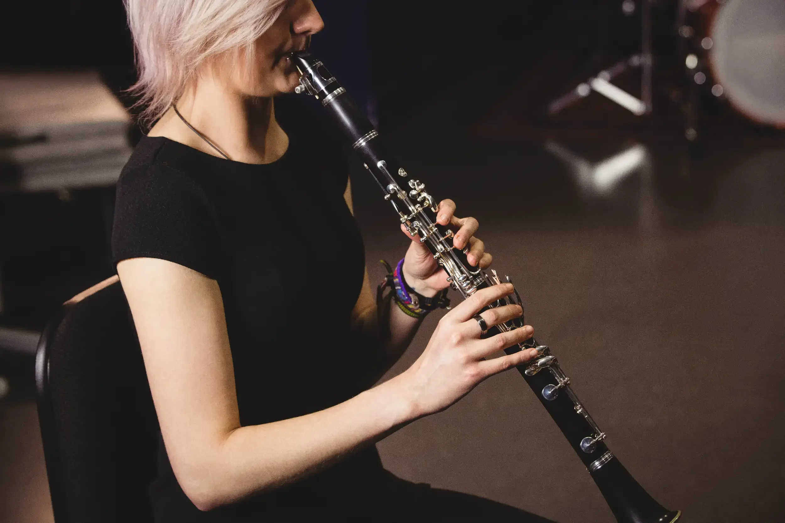 A woman with blonde hair playing a black clarinet in a dark room.