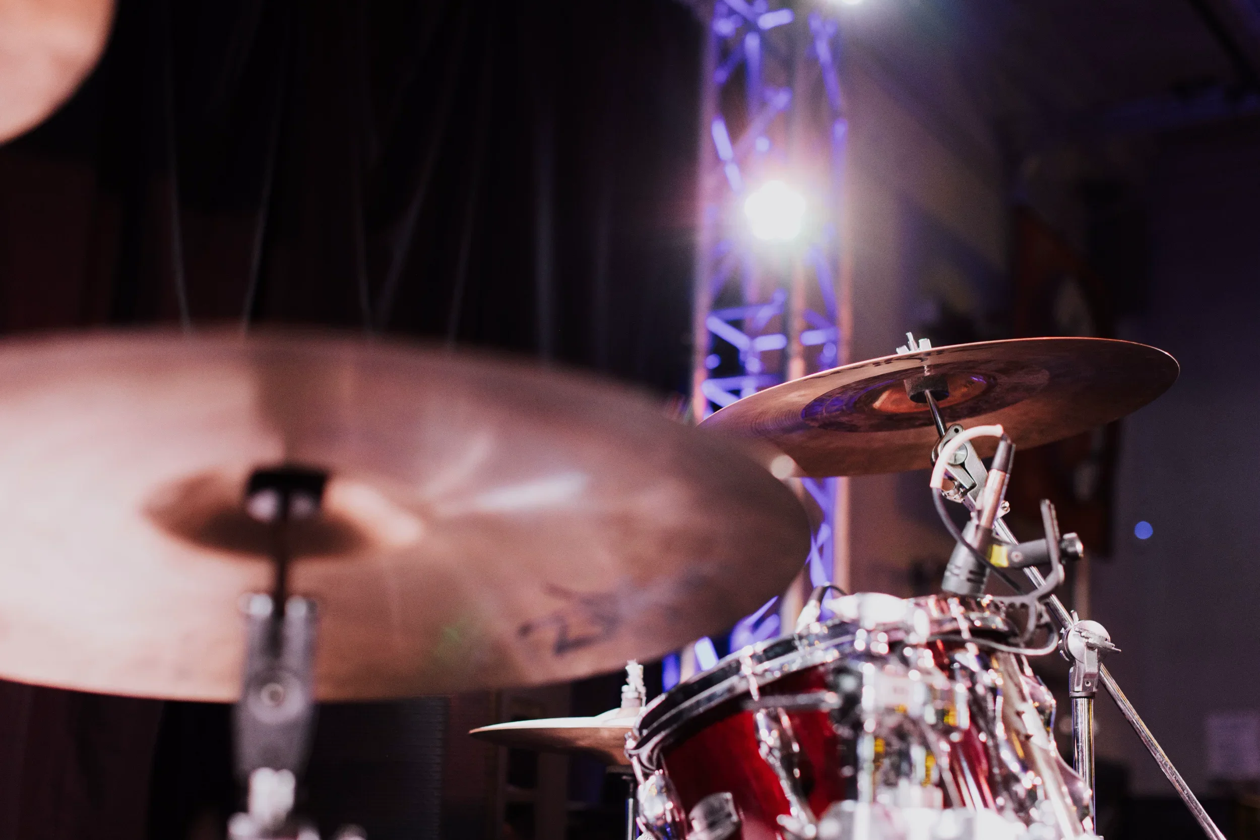 Close-up of a drum set with cymbals, with stage lights and truss in the background.