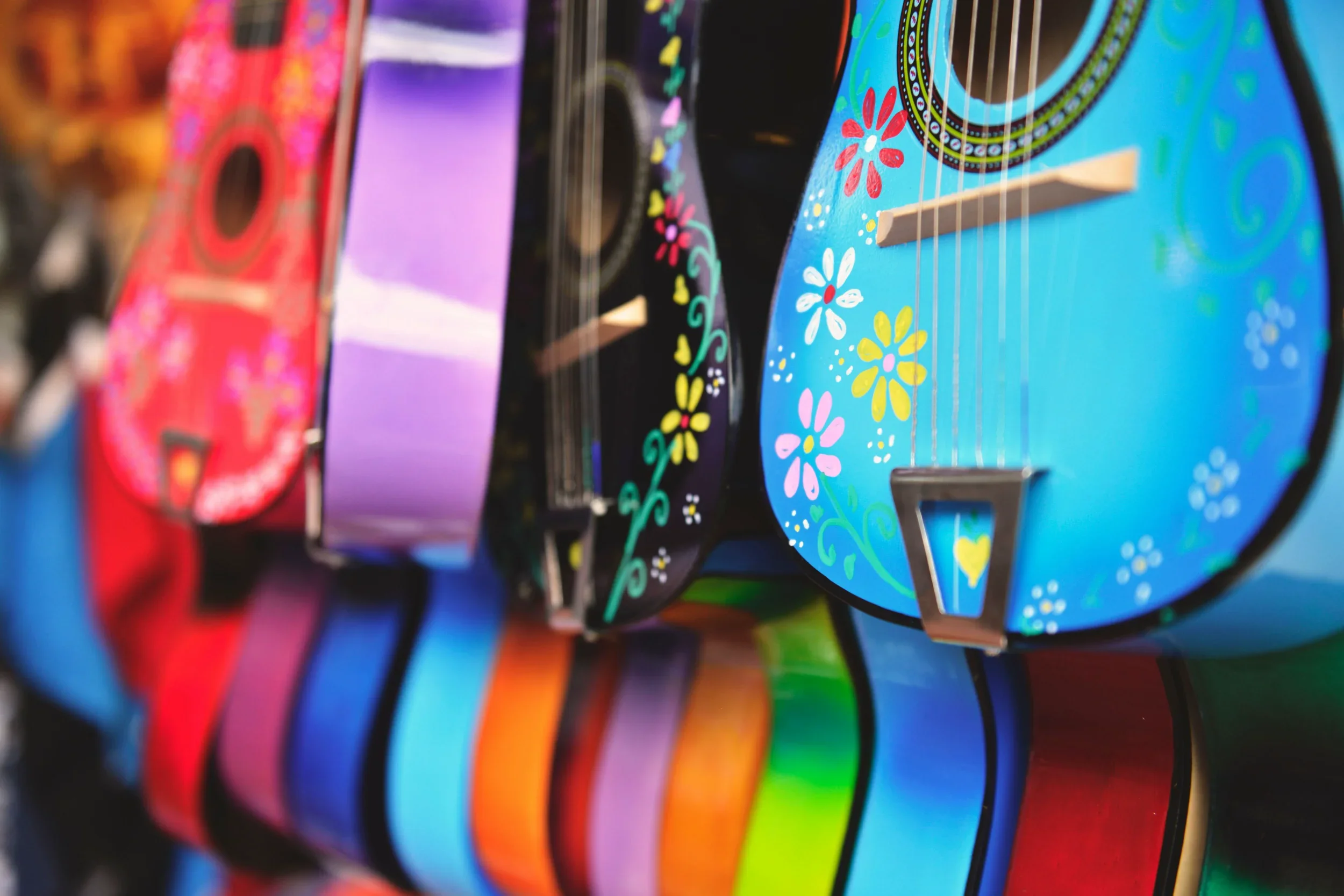 Close-up of several colorful guitars with painted floral patterns on their bodies, arranged in a row.