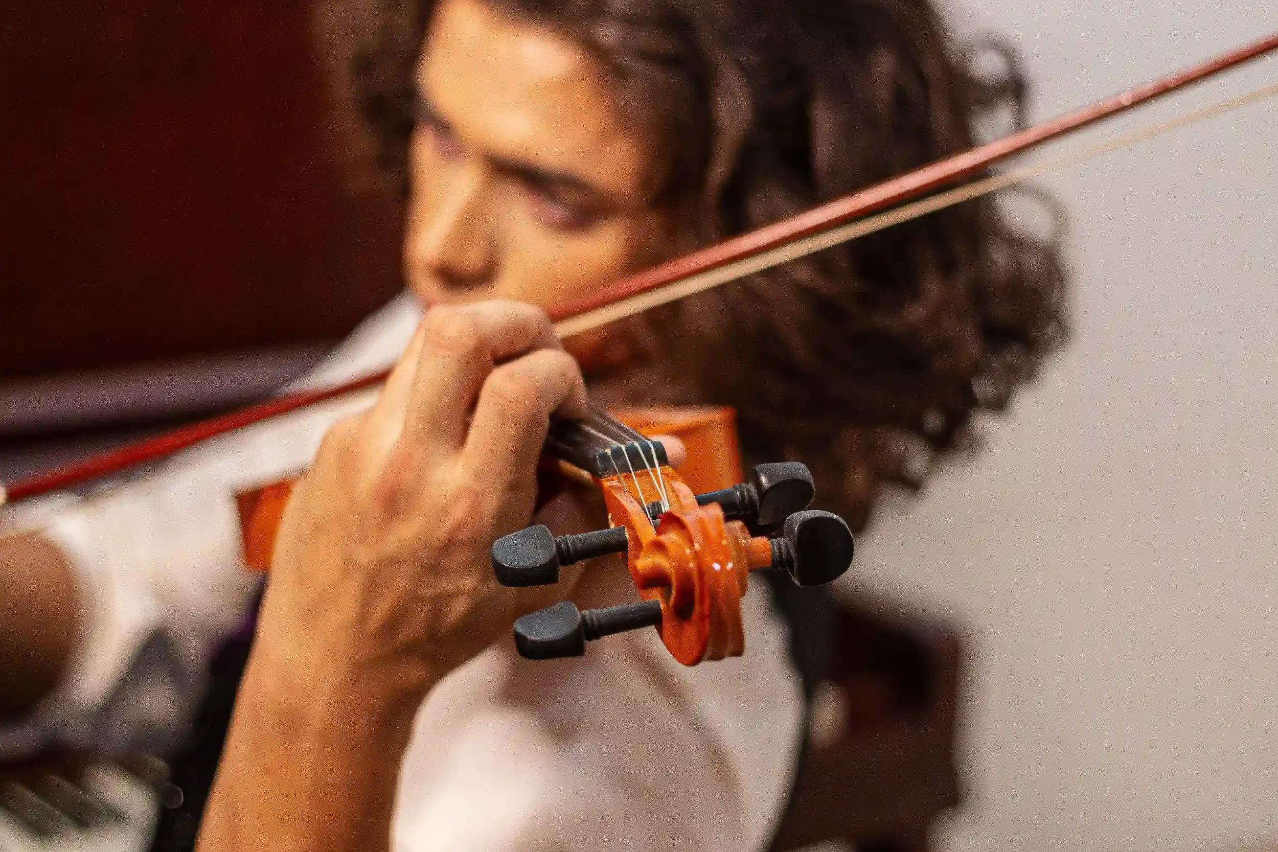 Close-up of a person playing a violin, focusing on the hand holding the bow and a part of the instrument.
