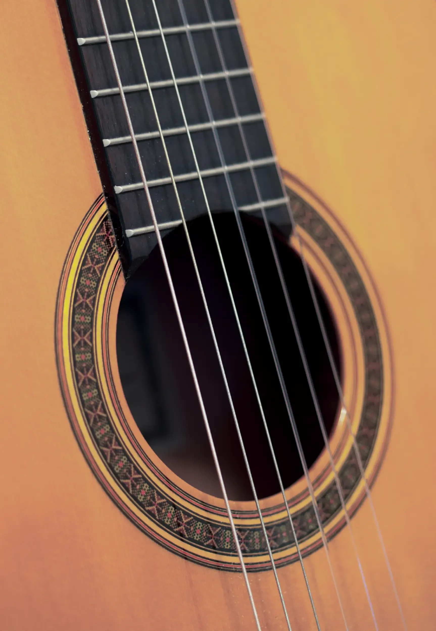 Close-up of an acoustic guitar's sound hole, strings, and rosette design on the body of the guitar.