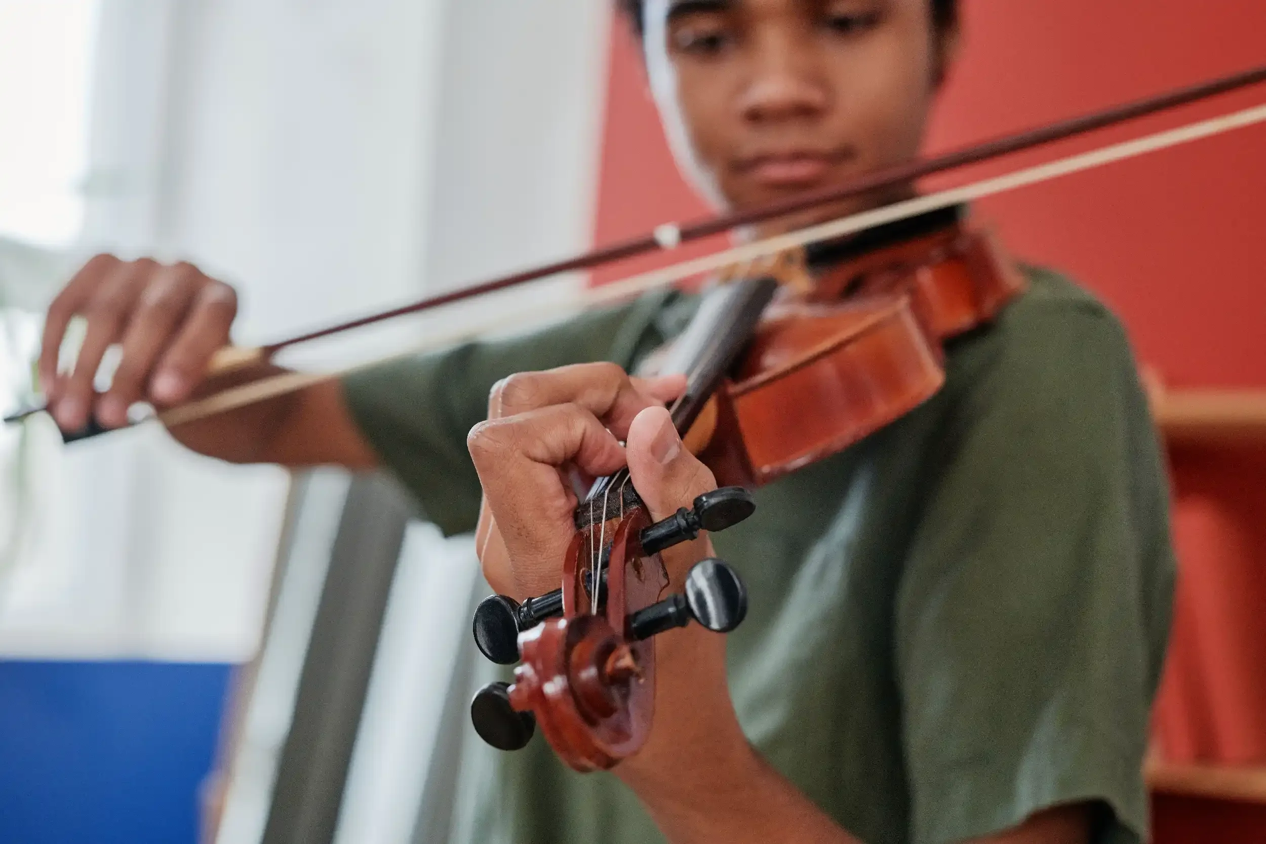 Person playing a violin, focusing on the violin and their hand on the fingerboard, with a blurred background.