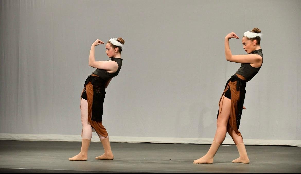 Two young women in dance costumes posing with flexed arm muscles on stage.