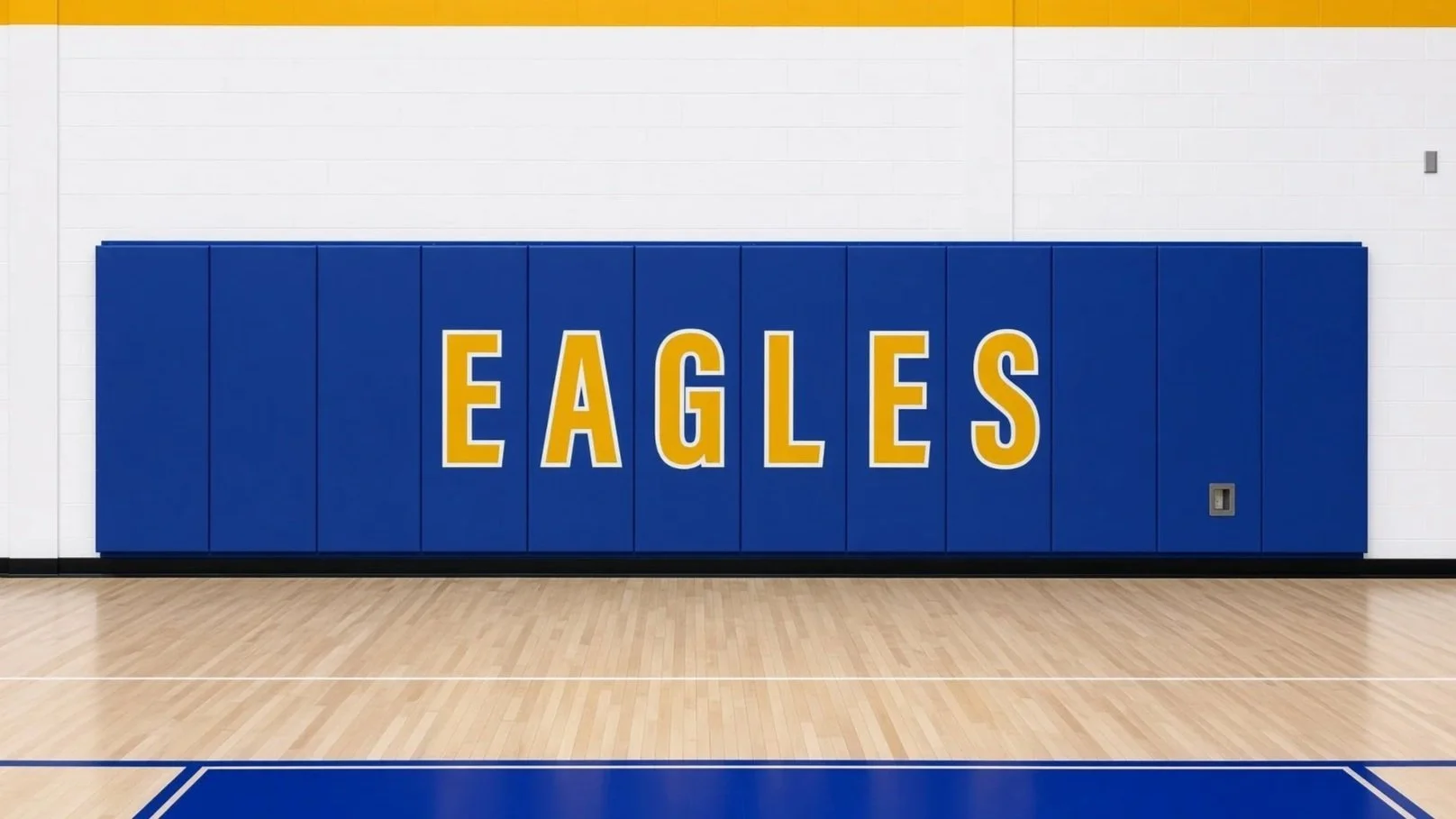 Indoor gymnasium with a blue padded wall display reading 'EAGLES' in yellow and white letters, hardwood floor, with blue and white markings.  Professionally installed casework or gym wall padding.
