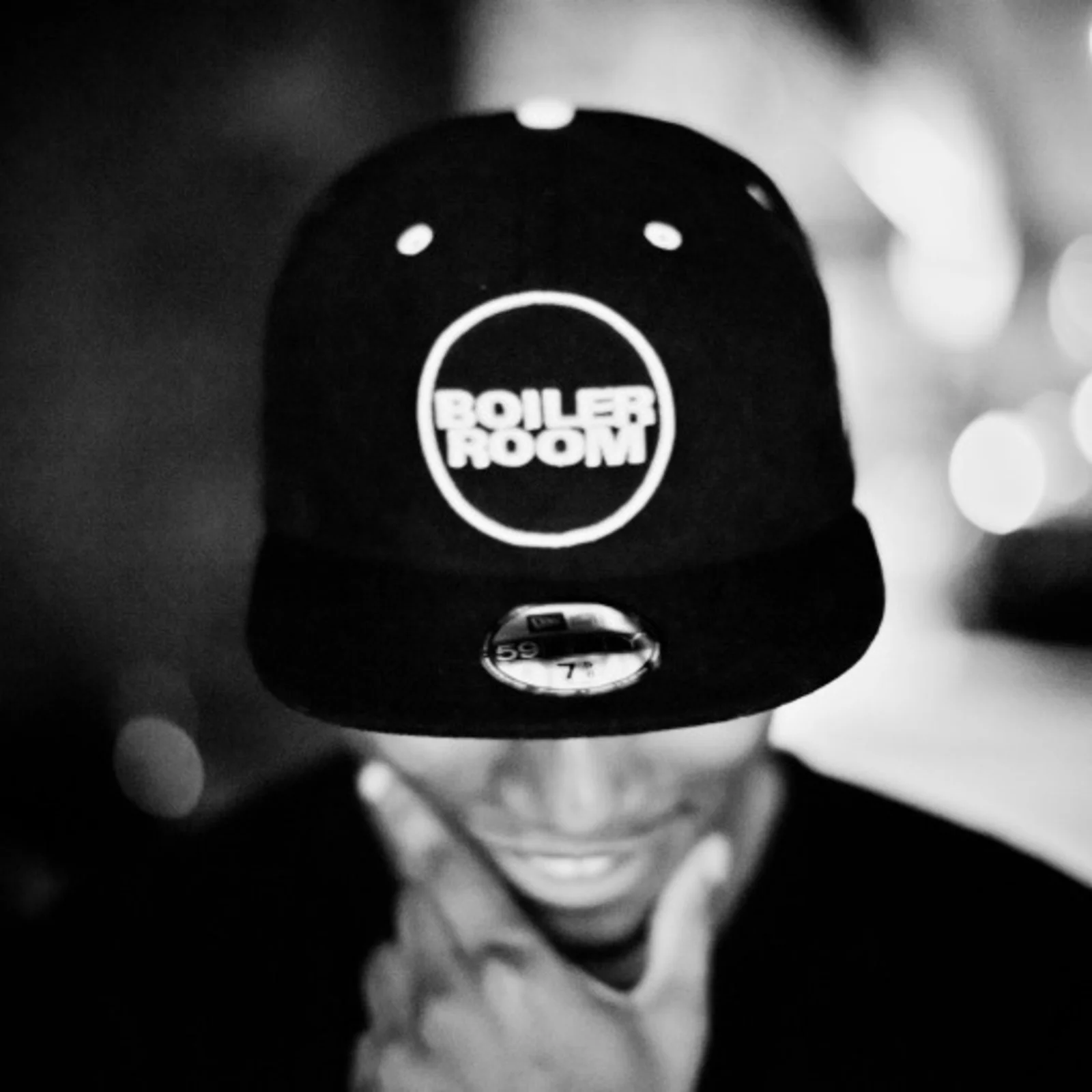 Person smiling while holding a cap with 'Boiler Room' logo on it