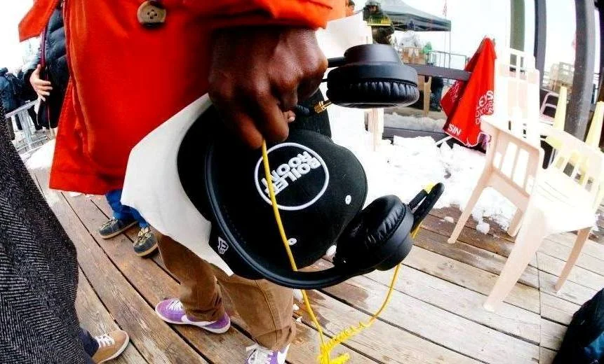 Person holding black headphones and a white sign with the logo '105.7 The Fan'.