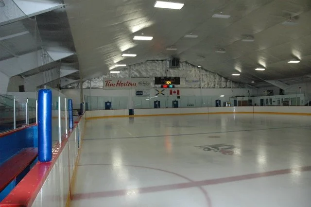 Empty indoor ice skating rink with benches on the side and a scoreboard above the ice.
