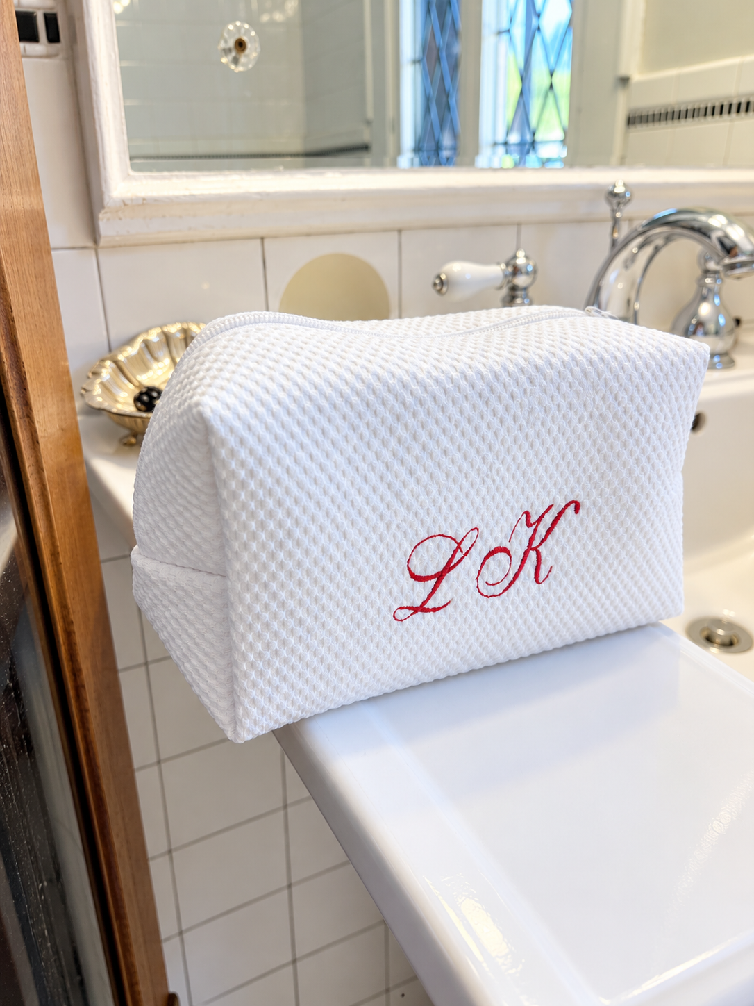 Monogrammed white waffle pouch with red embroidered initials on a marble bathroom counter