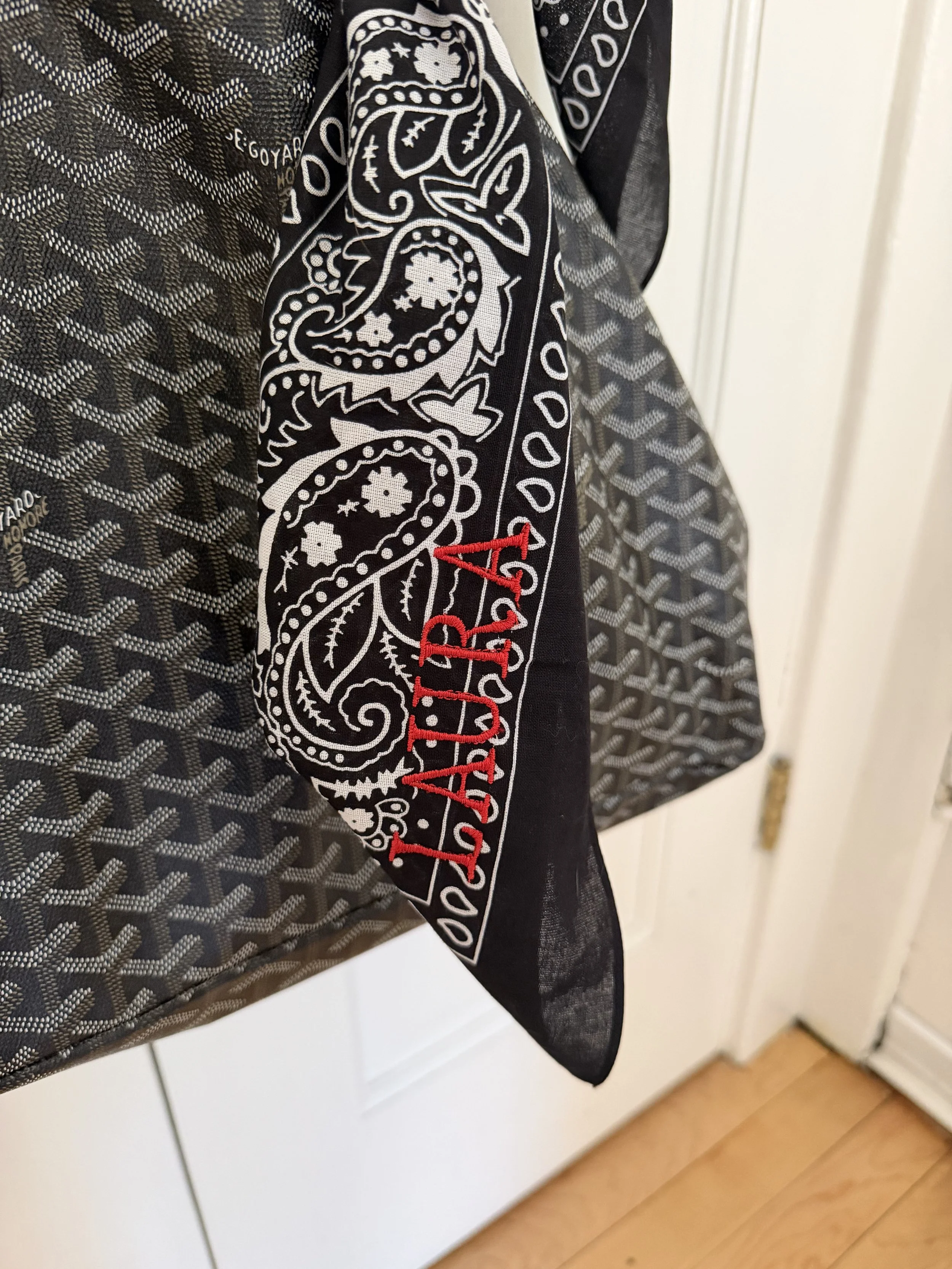 Close-up of red script embroidery on a navy paisley bandana knotted on a tote