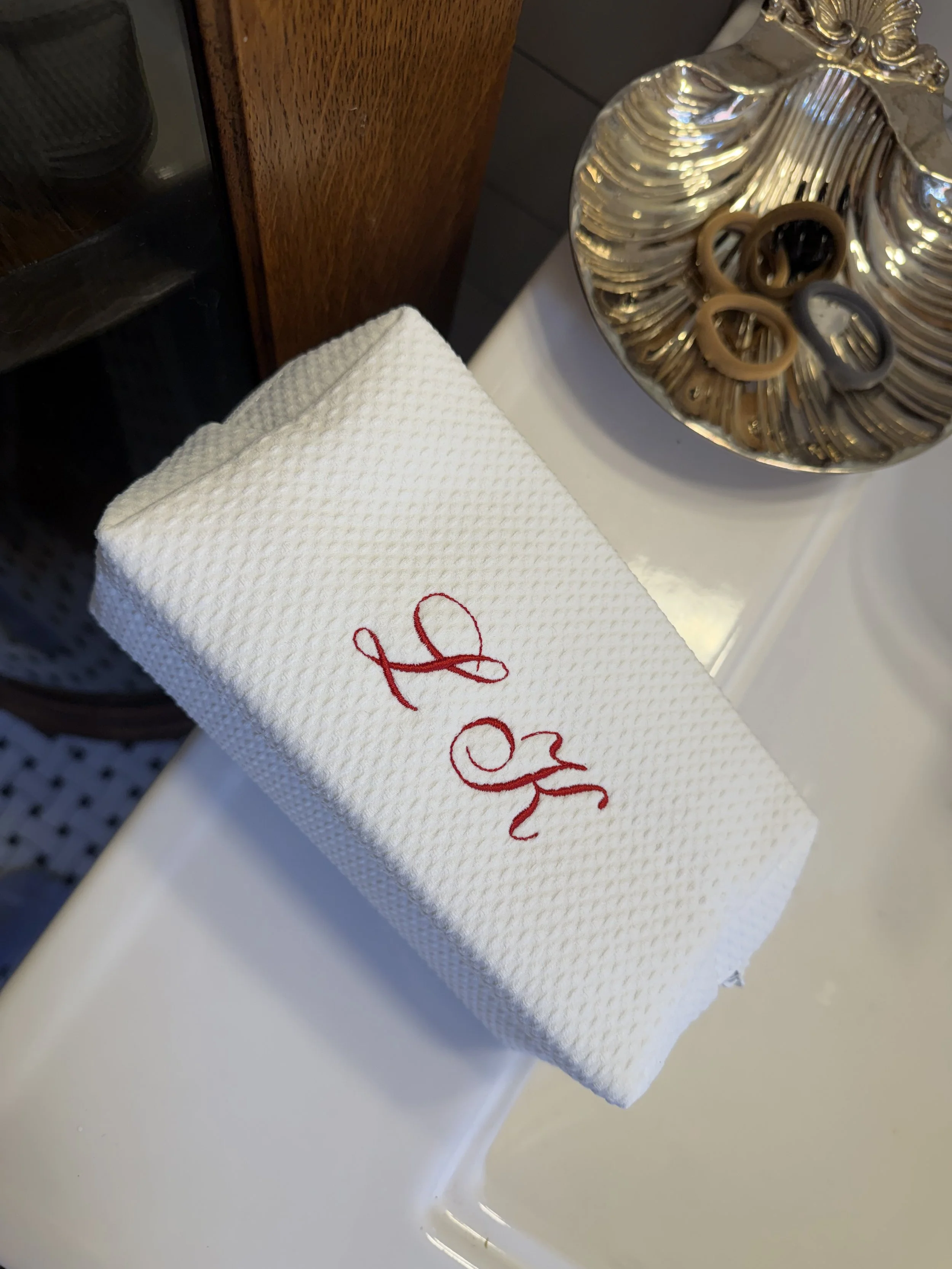 Close-up of red script LK monogram embroidered on a white waffle-weave cosmetic pouch