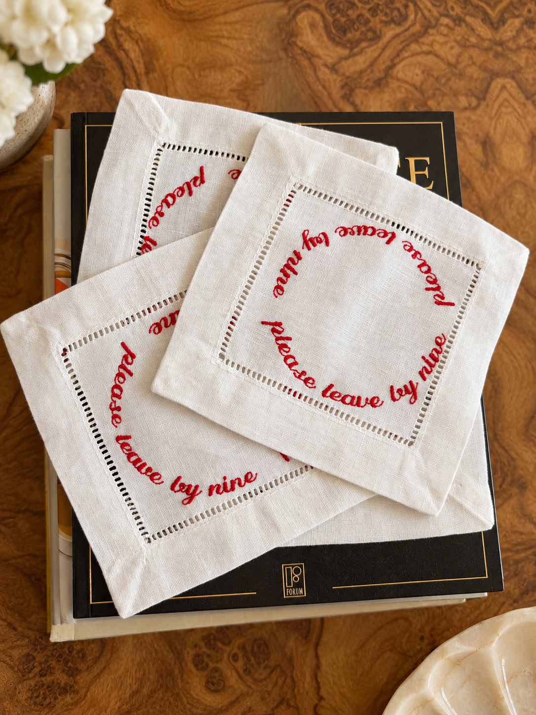The Please Leave at Nine Cocktail Napkins by The Linen Letter: four white hemstitched linen napkins with red embroidered lettering, stacked on a bar cart