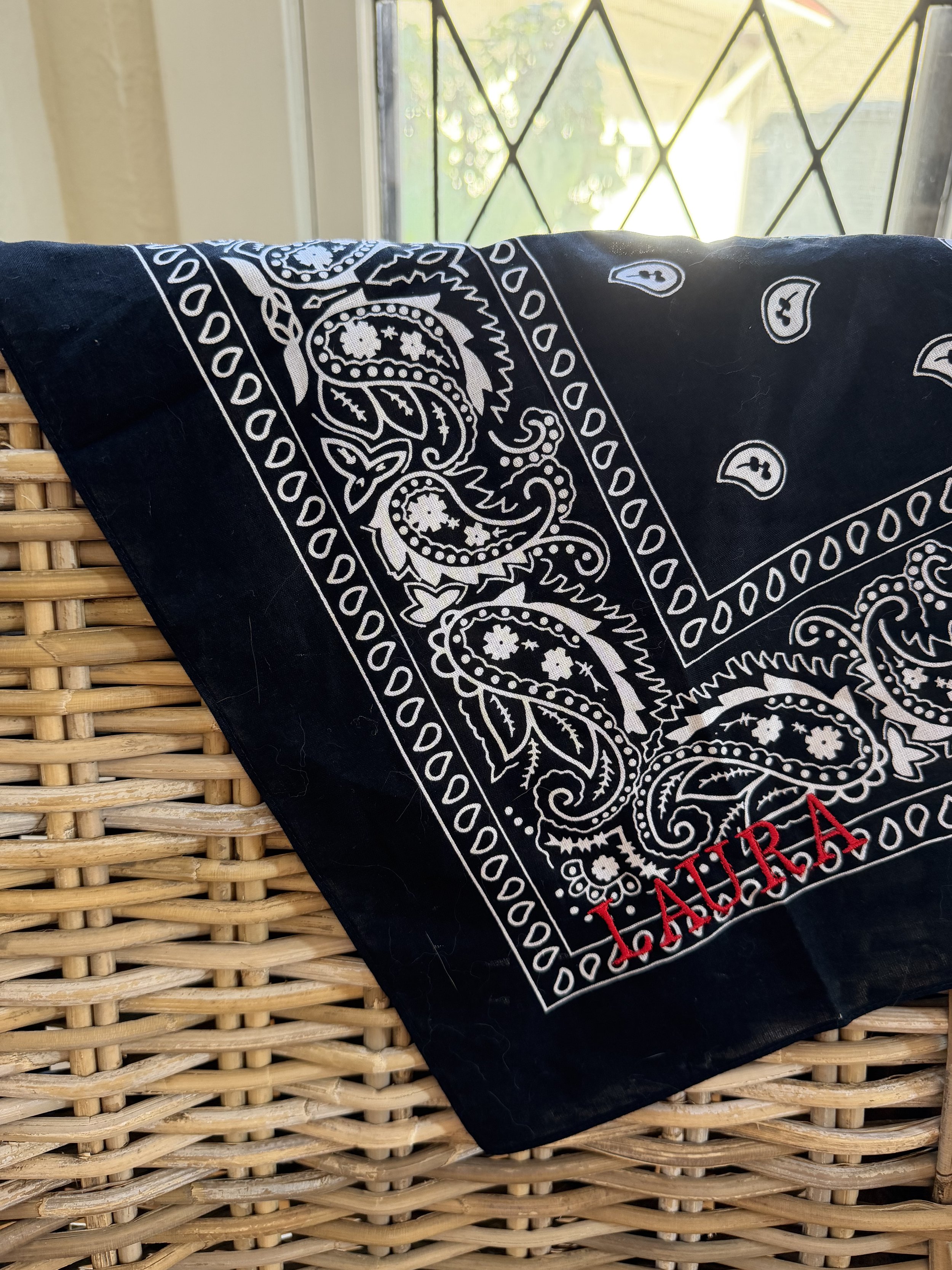 Navy paisley bandana with red embroidered name laid flat on a woven basket