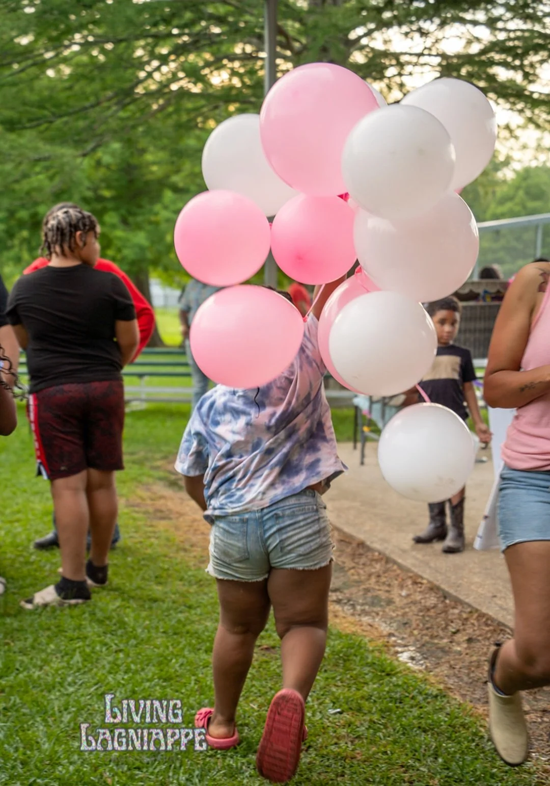 Child carrying pink and white balloons at a Legacy Loop Foundation community gathering.