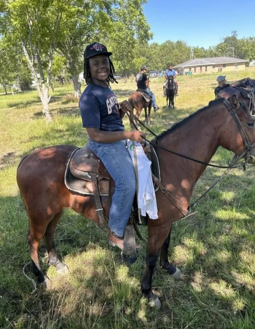 A smiling young rider seated on a brown horse at an outdoor Louisiana community gathering.