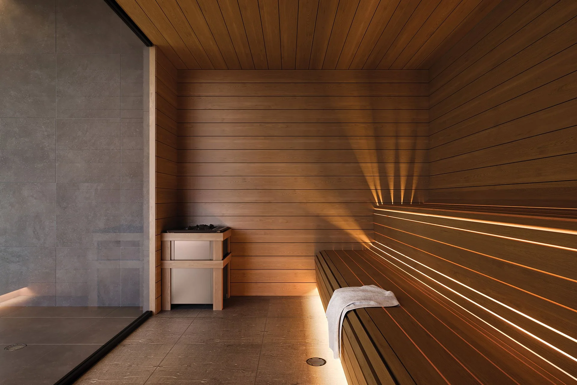 Une salle de sauna en bois avec un banc, un porte-serviette gris, et un coin avec des pierres de sauna, éclairée par des lumières chaudes.