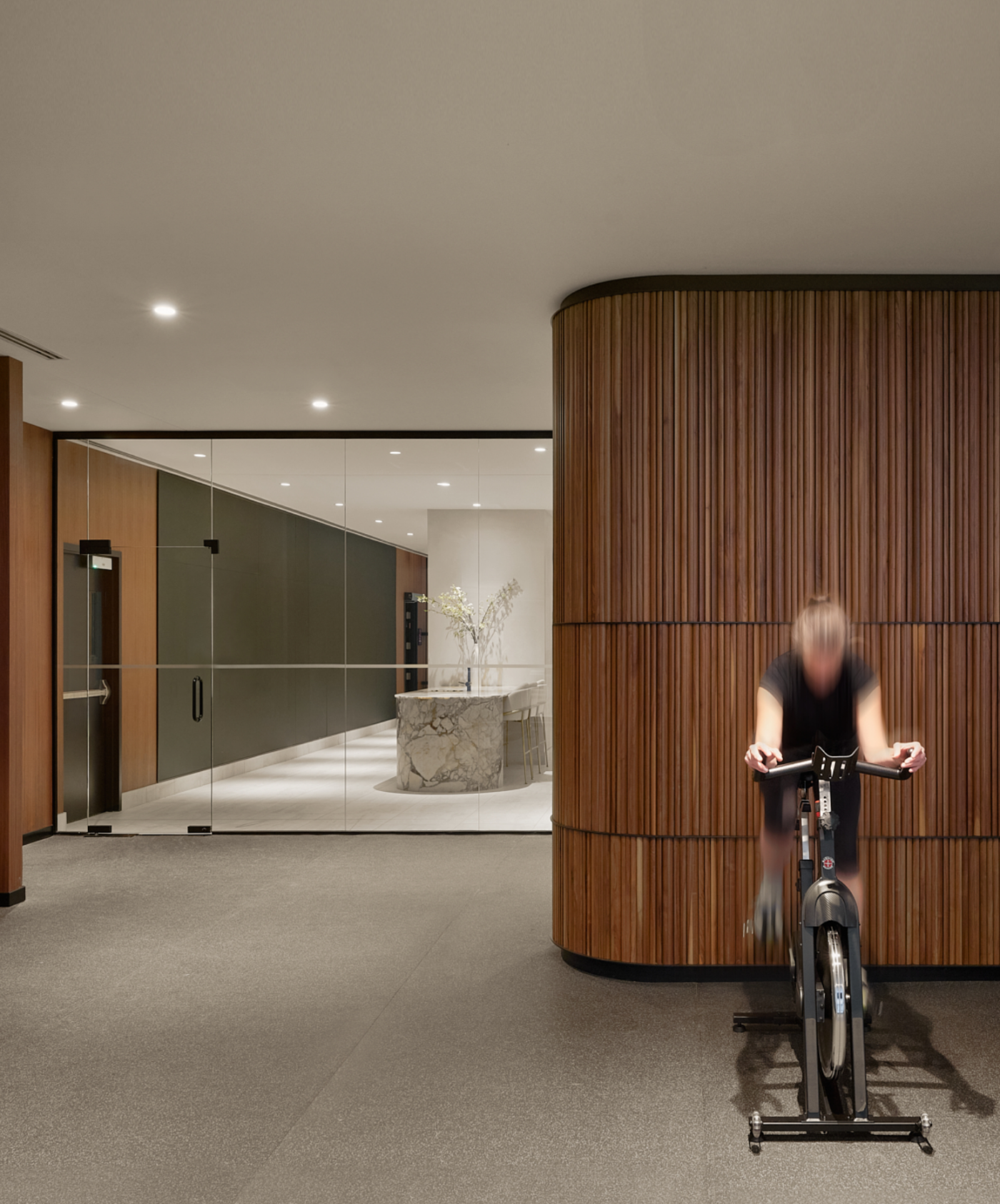 Une personne faisant du vélo d'appartement dans un hall moderne avec des murs en bois courbés et une section en verre noir.