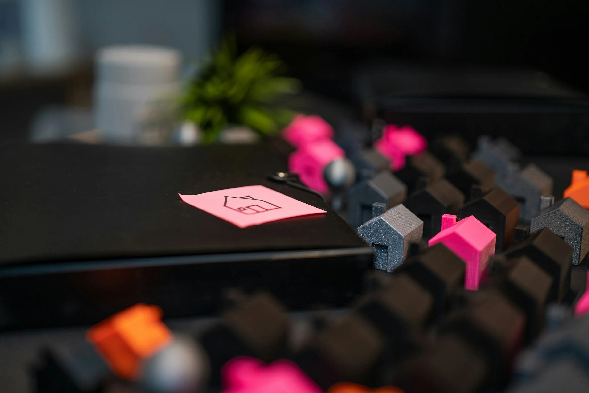 Close-up of a computer keyboard with black keys and colorful keycaps, including pink ones, and a sticky note with a house symbol.