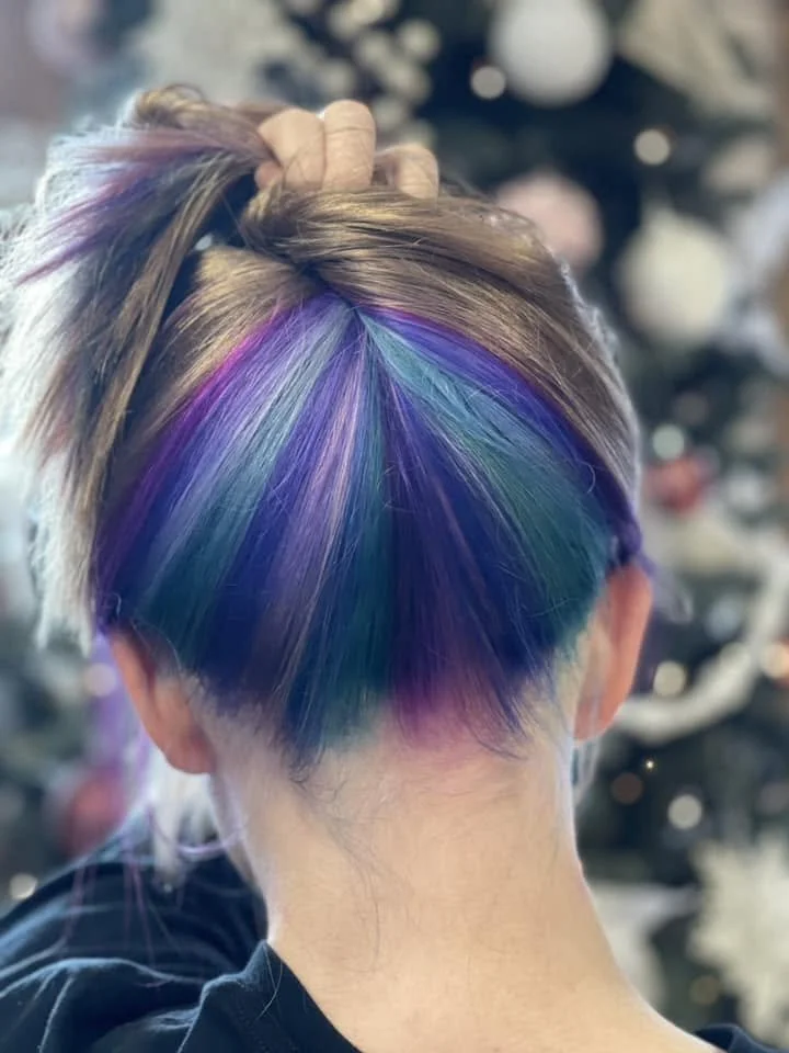 Back view of a person's head with colorful rainbow blue and purple highlights in short hair, tied up with a hand. Colorist. FABCO Fallon Aliece Beauty CO. Eagle River. WI. 