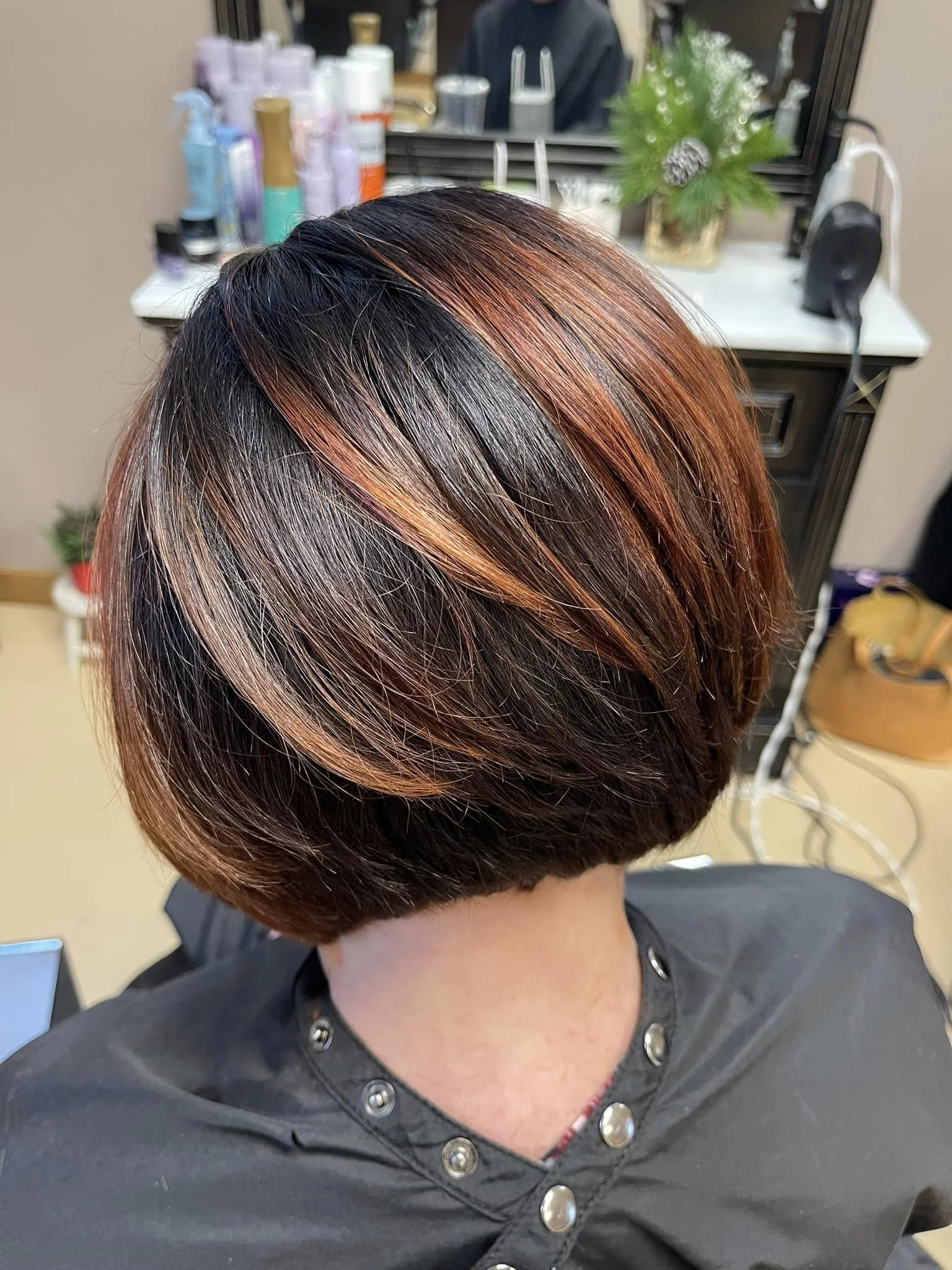 Close-up of a person's styled short bob haircut with black and reddish-brown highlights, worn by someone in a salon setting at Falon Aliece beauty Co. Eagle River, WI 