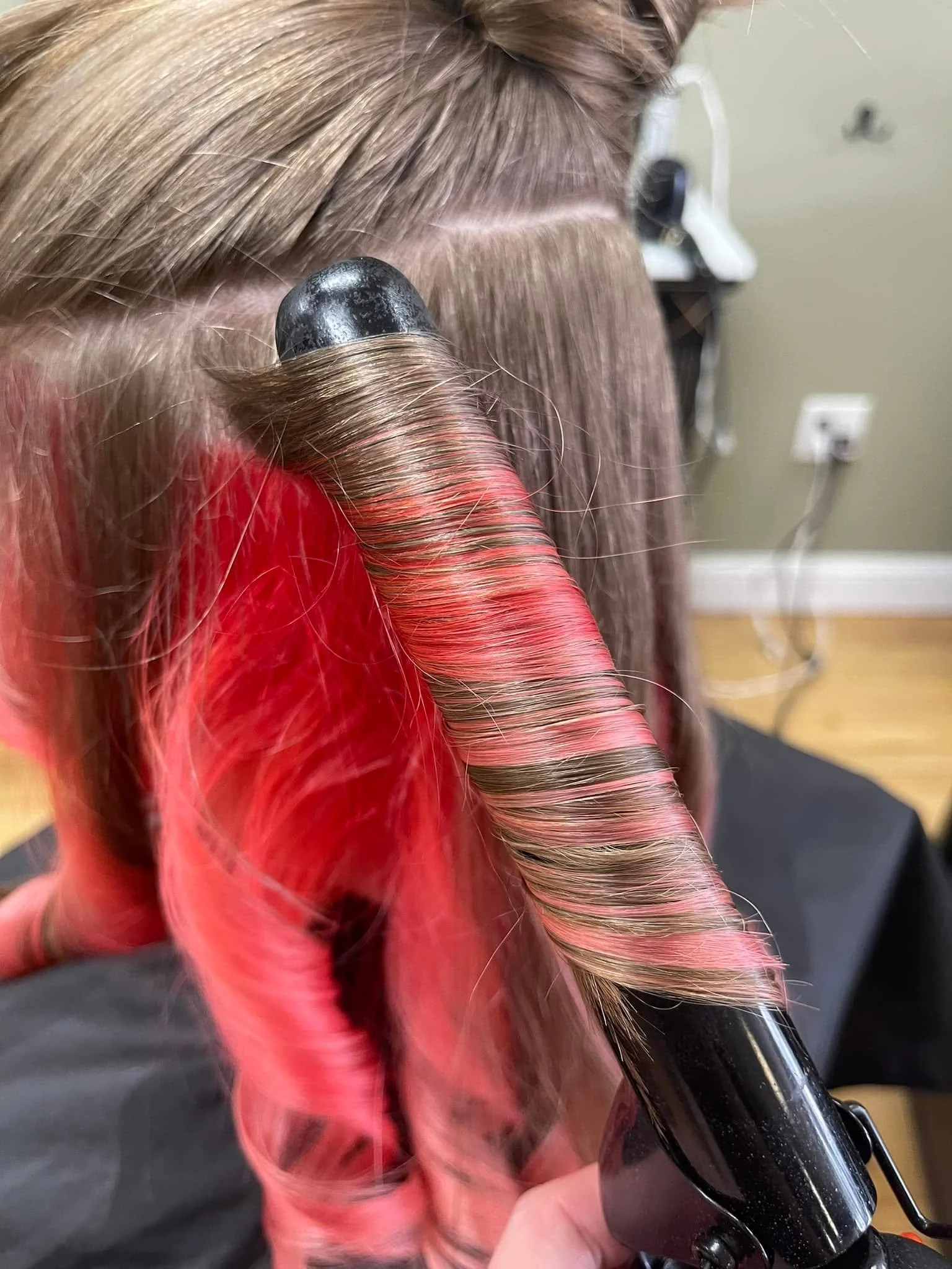 Close-up of a person with curled blonde hair, using a curling iron to style hair.