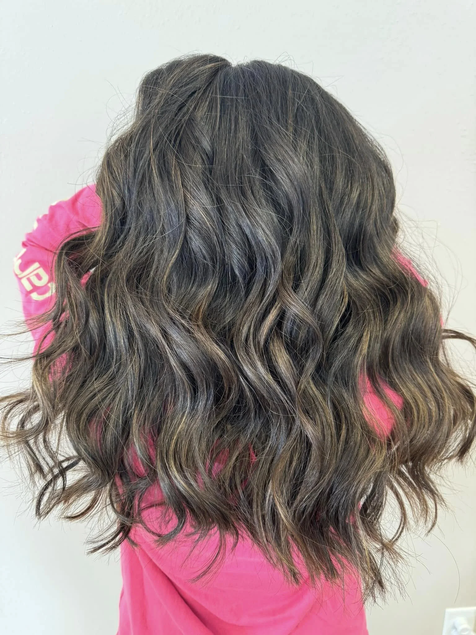 A person with long, wavy hair that has highlights of brown and blonde, wearing a pink top. Hair styles. Colorist. Eagle River, WI FABCO salon.