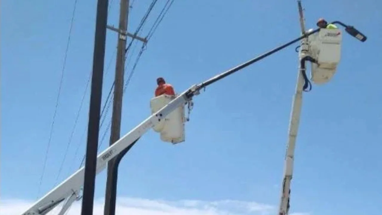 Two utility workers in safety gear working on electrical lines from a bucket lift against a blue sky.
