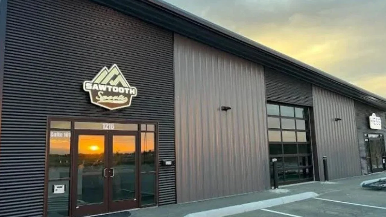 Exterior of a modern industrial-style sports facility with a sign that reads 'Gawth Sports'; sunset reflected in glass door windows.