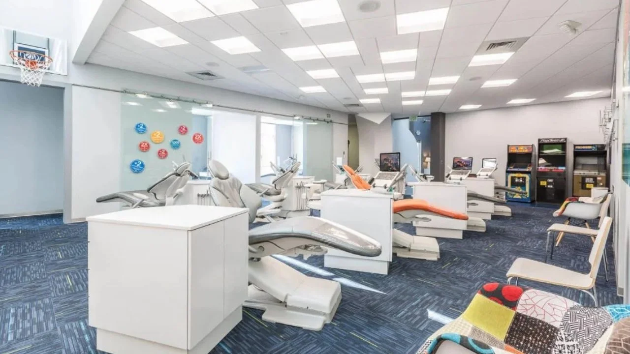 Dental clinic with multiple dental chairs, monitors, and arcade machines in the background.