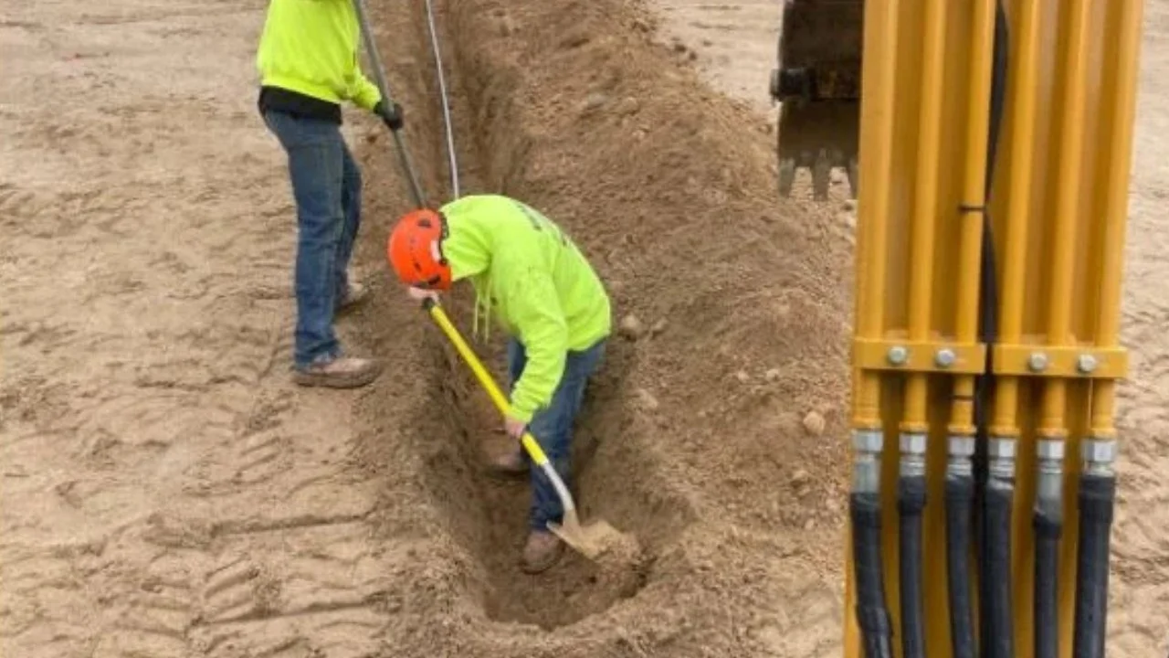 Two construction workers in safety gear digging a trench at a construction site.