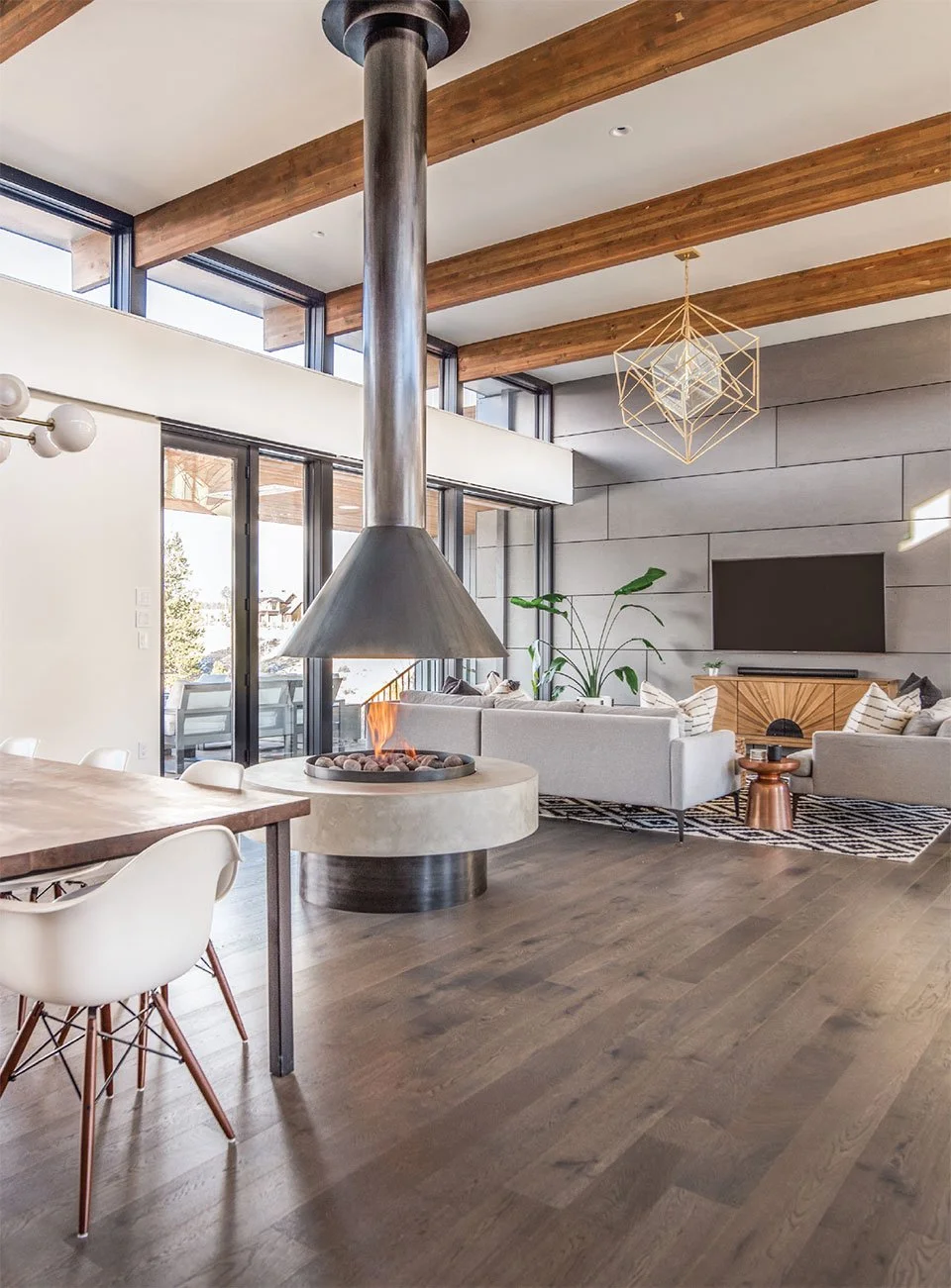 Modern open-concept living and dining room with large windows, a central fireplace, white sofas, wooden beams on the ceiling, and contemporary decor.