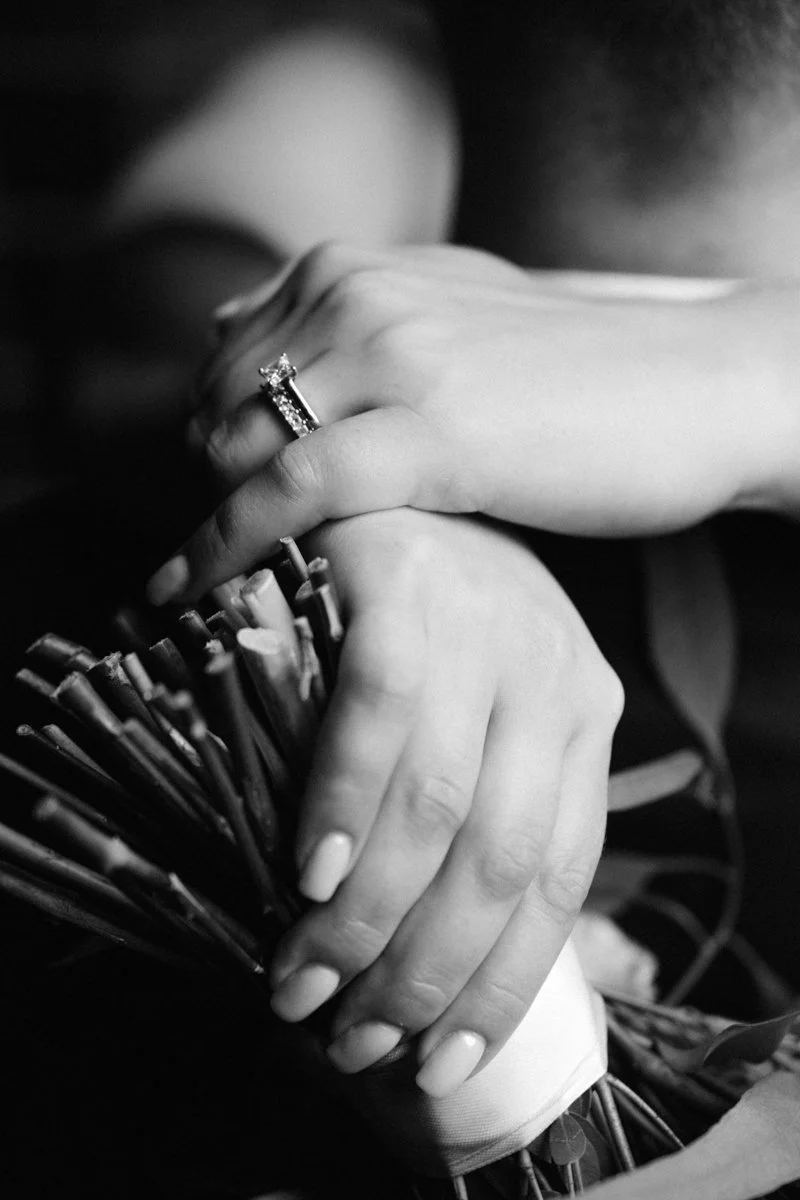 Close-up of a woman's hand with an engagement ring resting on a bouquet of flowers.