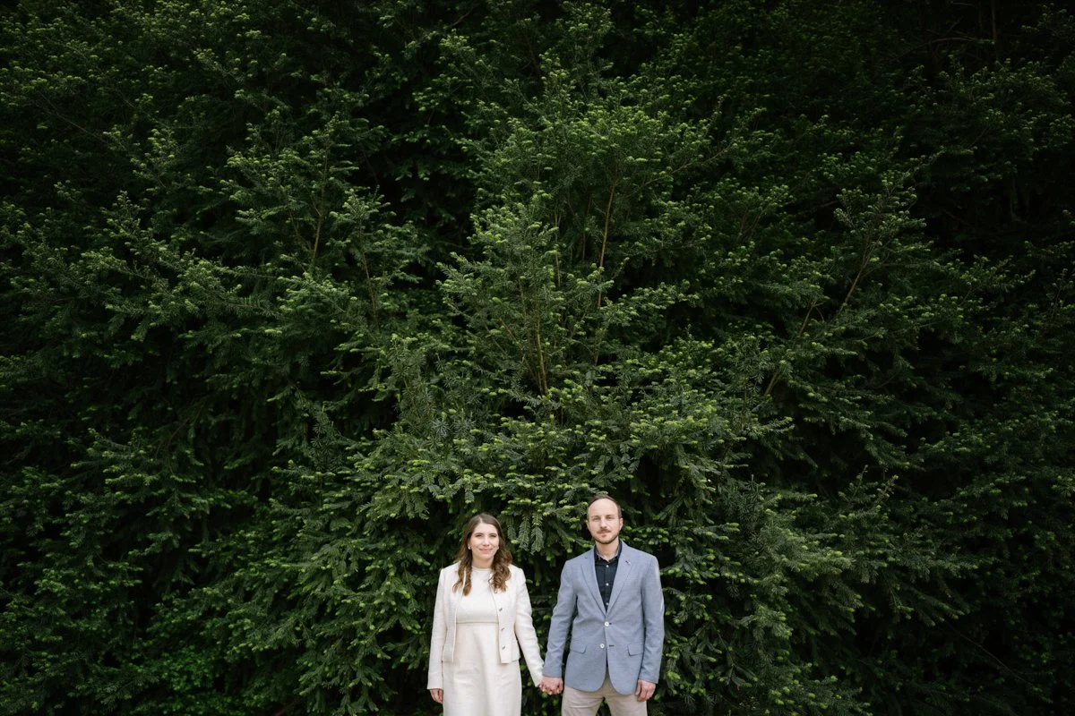 A woman and a man holding hands in front of a large green tree.