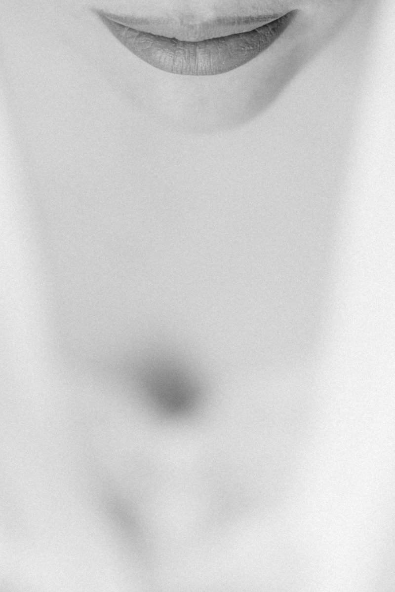 Close-up of a person's lips with a faint shadow of facial features, in black and white.