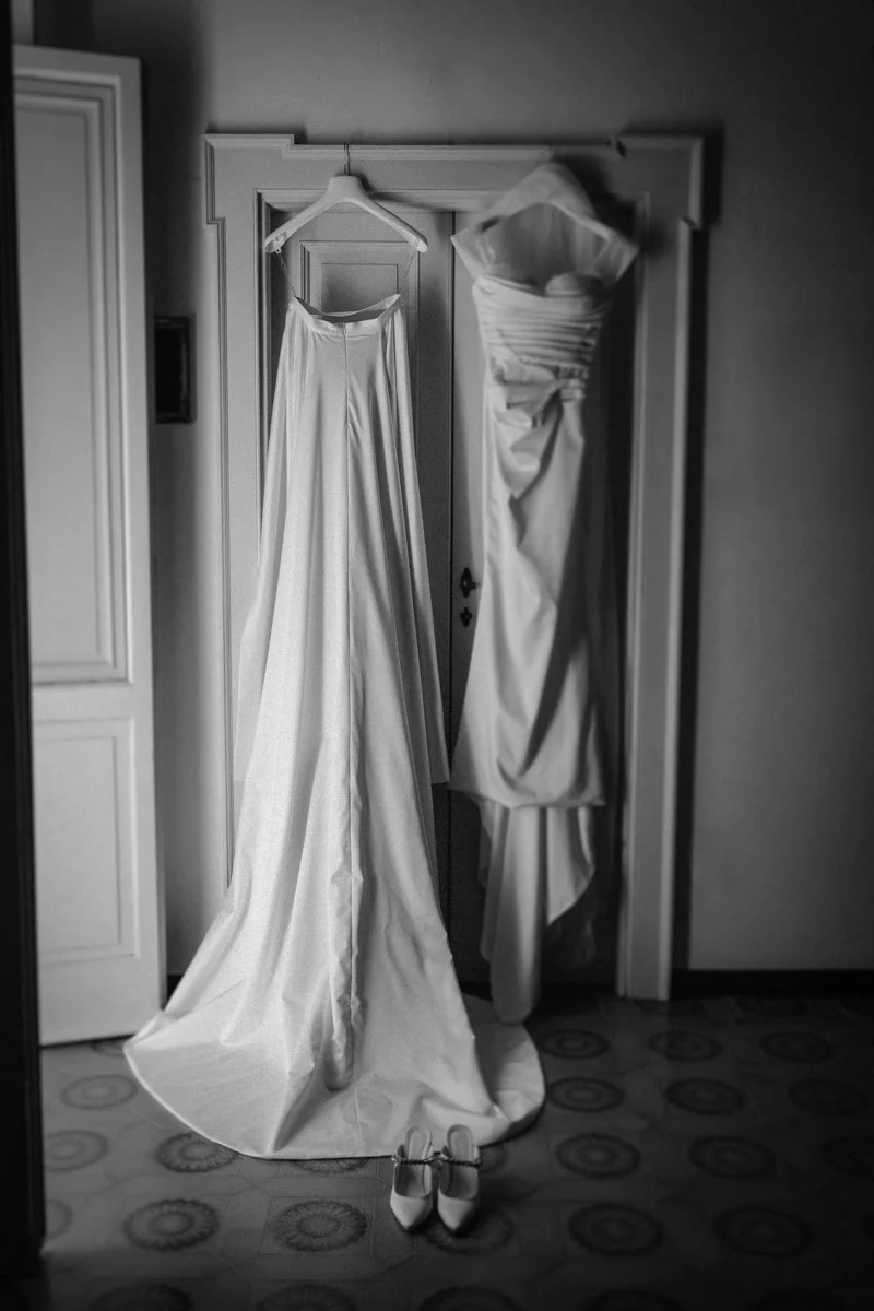 A wedding dress hanging on a hanger, and a wedding gown hanging in a closet, with a pair of heels on the floor underneath.