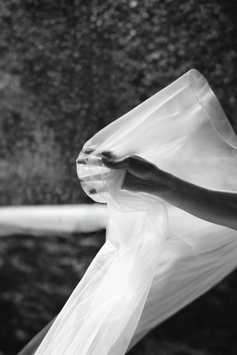 Black and white photo of a hand holding a transparent plastic or fabric sheet outdoors.