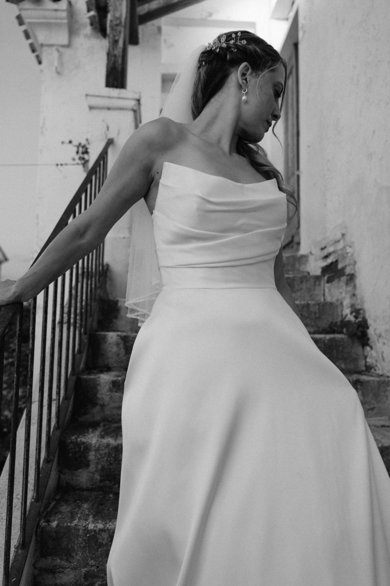 A woman in a wedding dress standing on a staircase with a railing, looking down, with an industrial background.