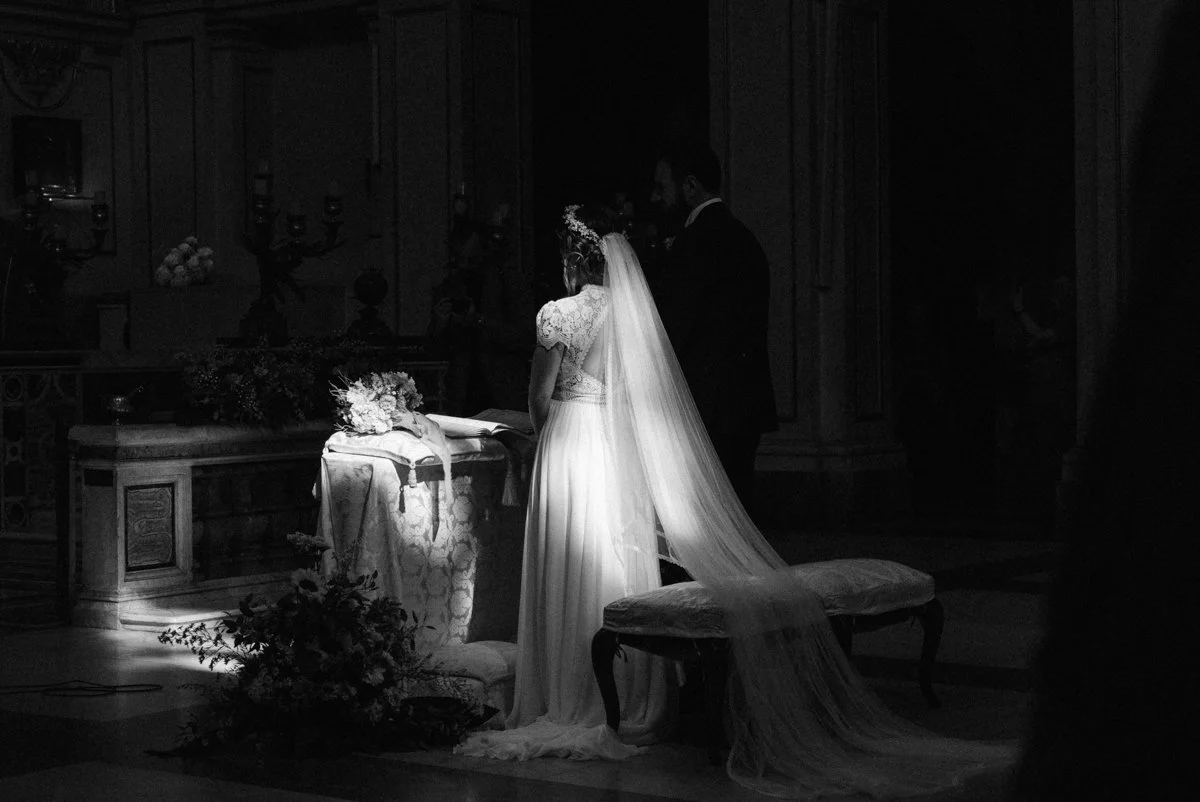 A bride and groom standing at the altar during a wedding ceremony, with the bride wearing a long dress and veil.