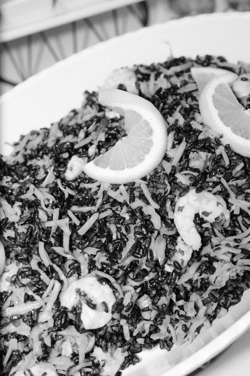 Black rice dish garnished with lemon slices and shredded cheese.