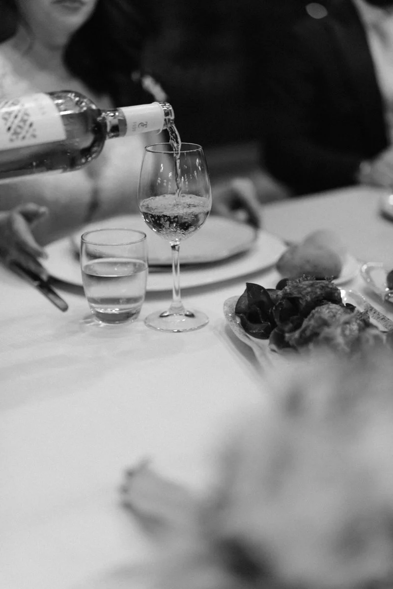 A person pouring a clear beverage into a wine glass at a dinner table with various plates and glasses.