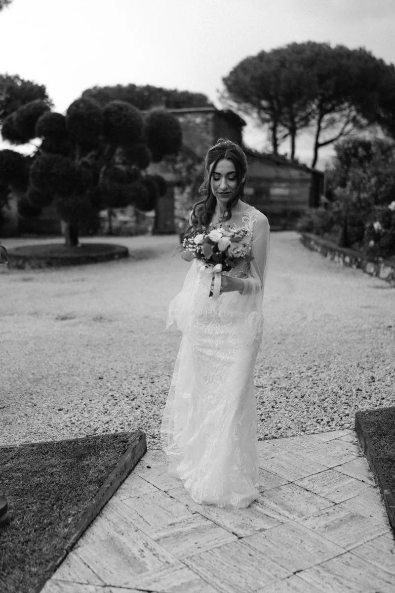 A woman in a wedding dress holding a bouquet of flowers outdoors.