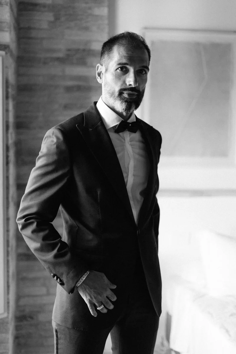 A man in a tuxedo with a bow tie standing indoors in a black-and-white photo.