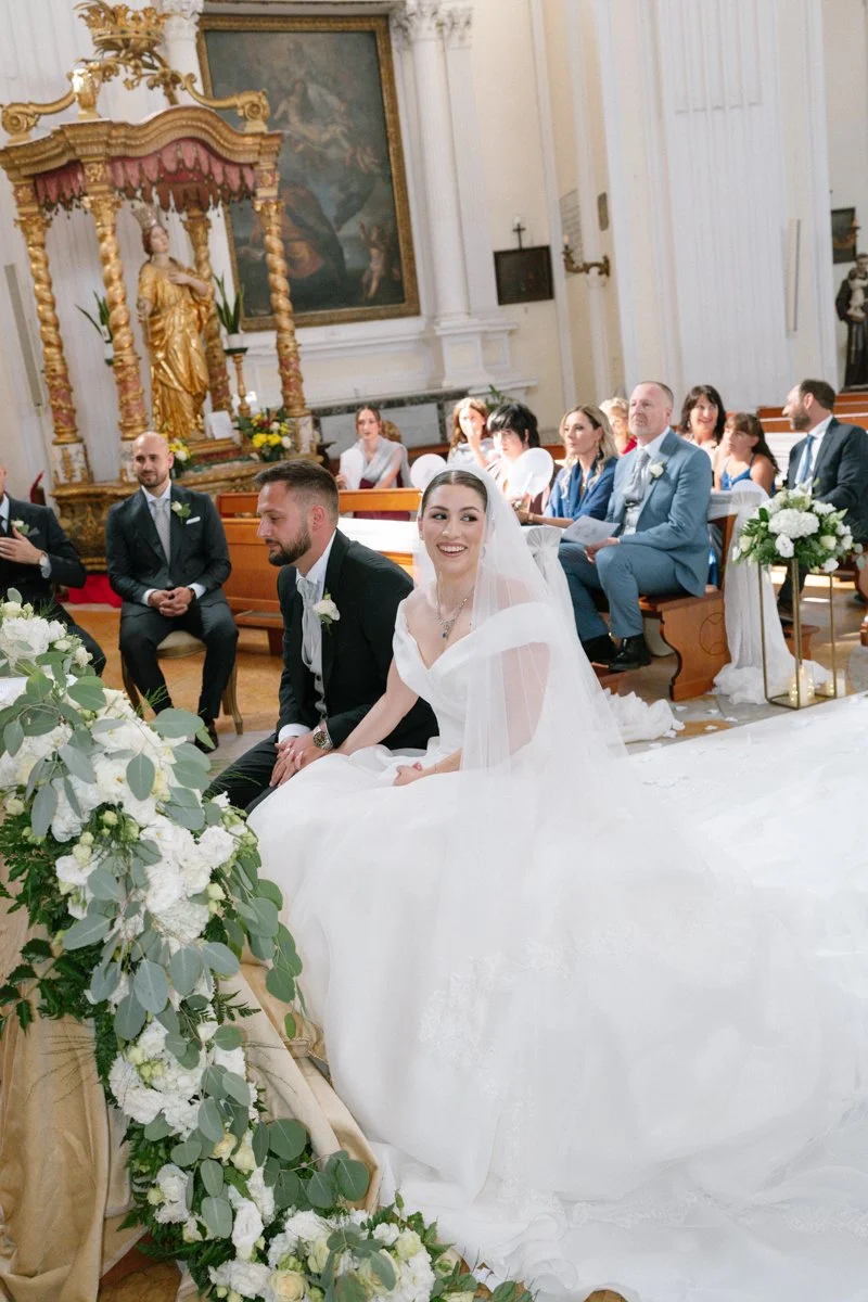 Bride and groom sitting at the altar during a wedding ceremony inside a church.