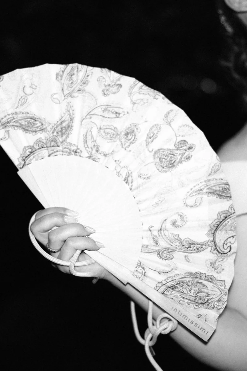 A person holding a decorative folding hand fan with a paisley pattern.